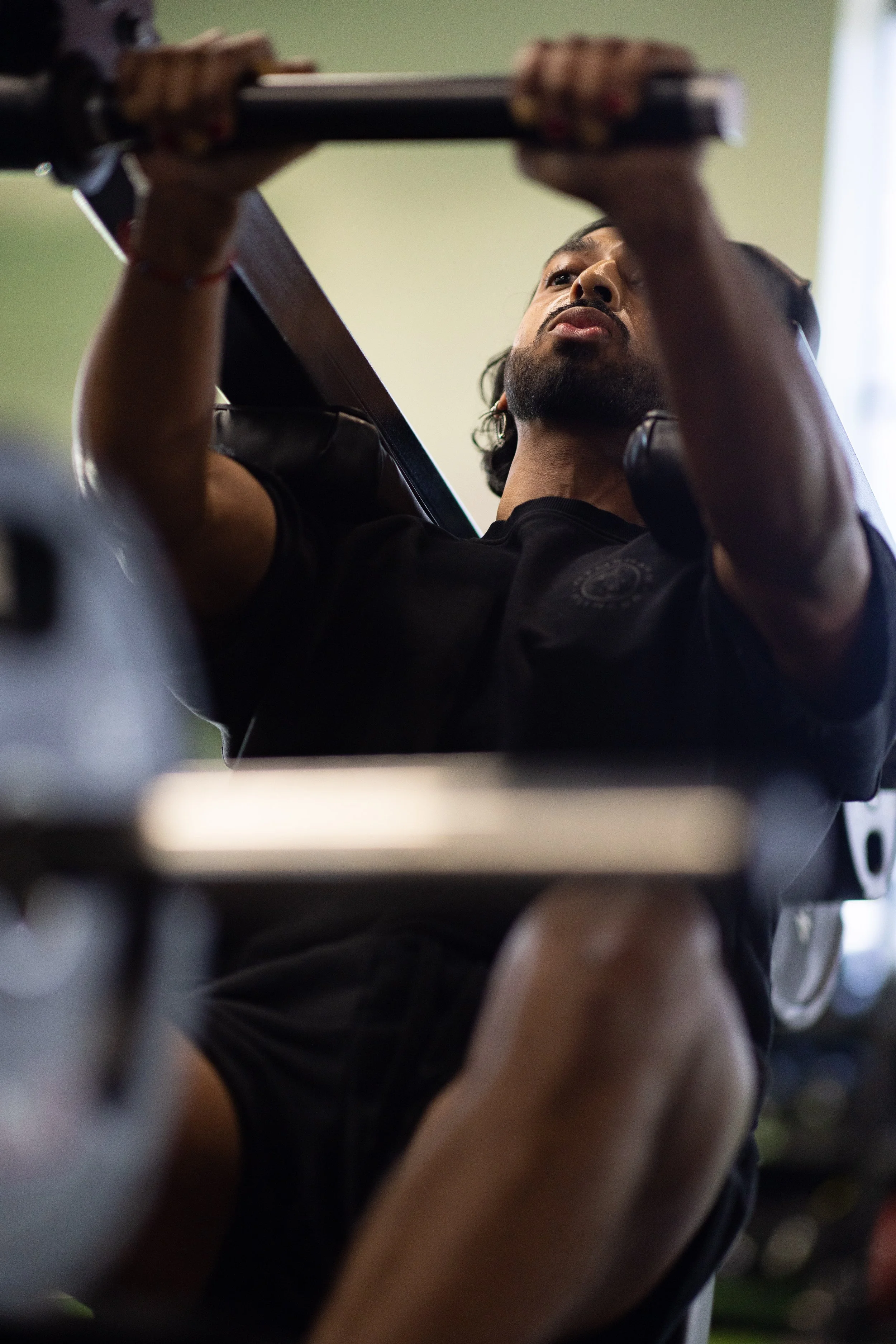 Man lifting weights on a bench in a gym, focusing on his upper body and face.