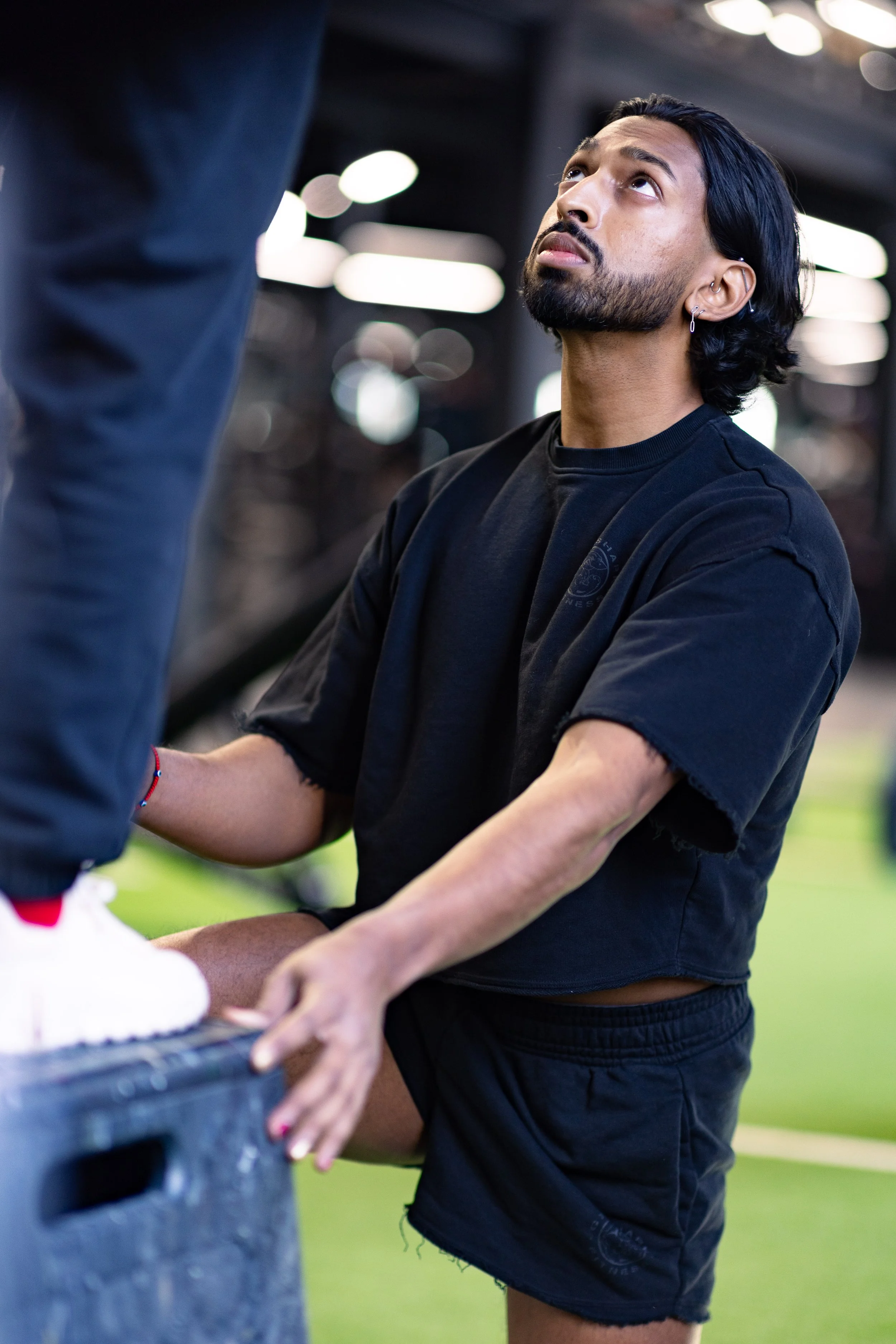 A man kneeling on one knee while receiving a kick to his thigh during a training session, with a focused expression.