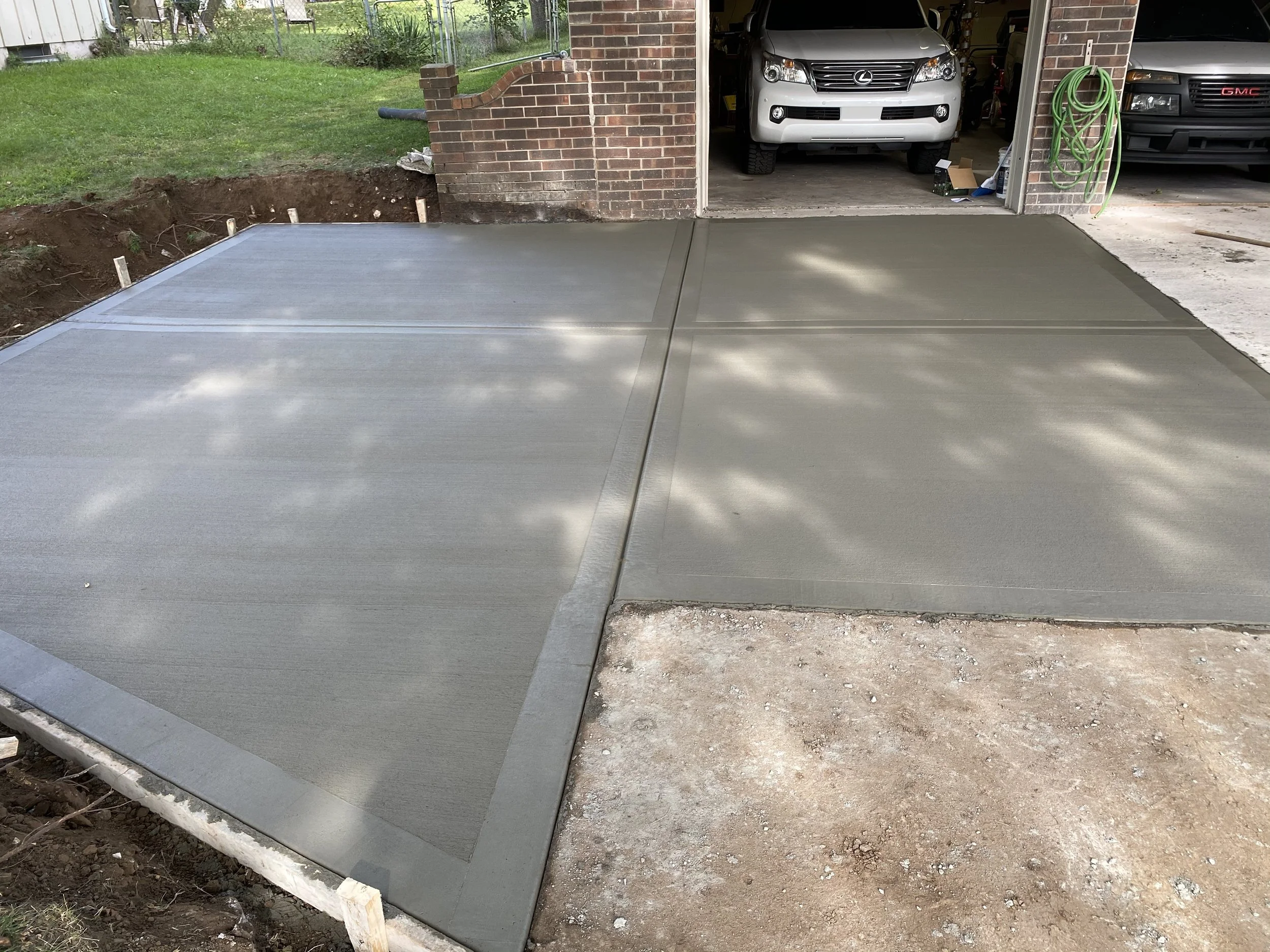 Recently poured concrete driveway in front of a garage with vehicles parked inside