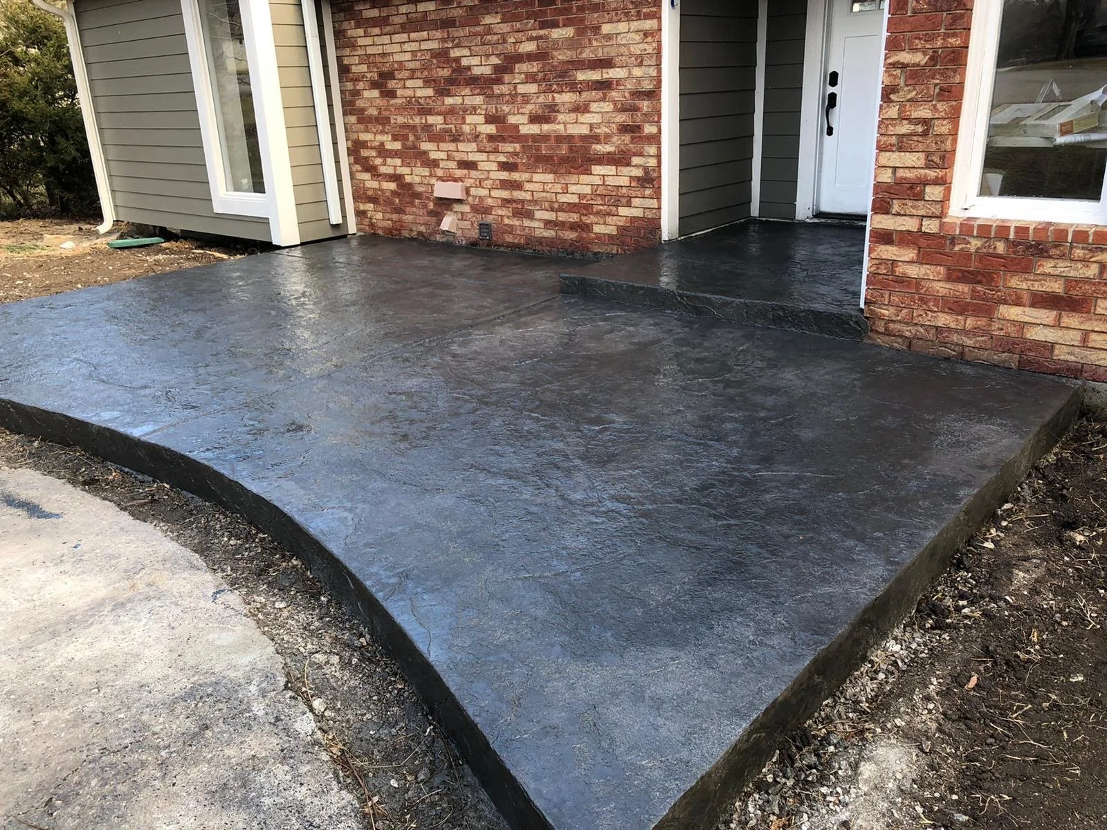 Newly poured concrete porch with black edging in front of the house, with a step leading to the door.