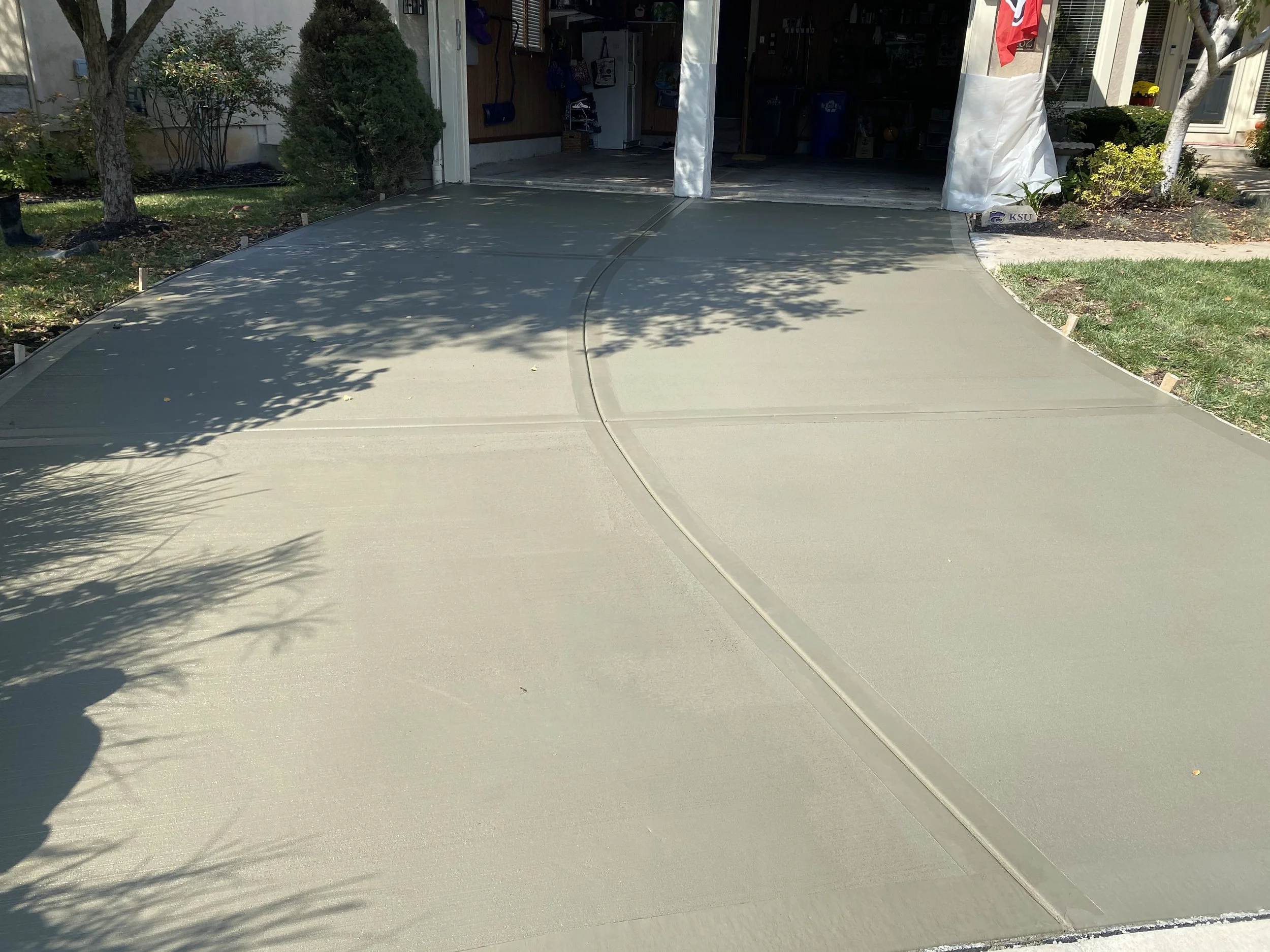 Freshly poured concrete driveway in front of a garage, with some shadows from trees and landscaping on the surface.