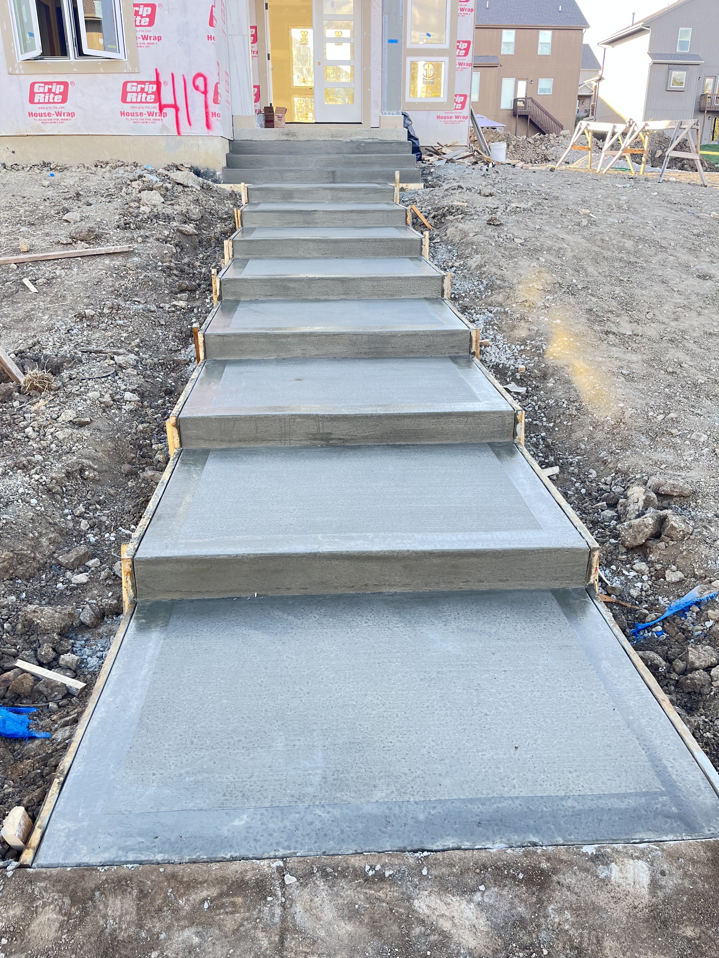 Concrete sidewalk with steps leading to a house under construction.