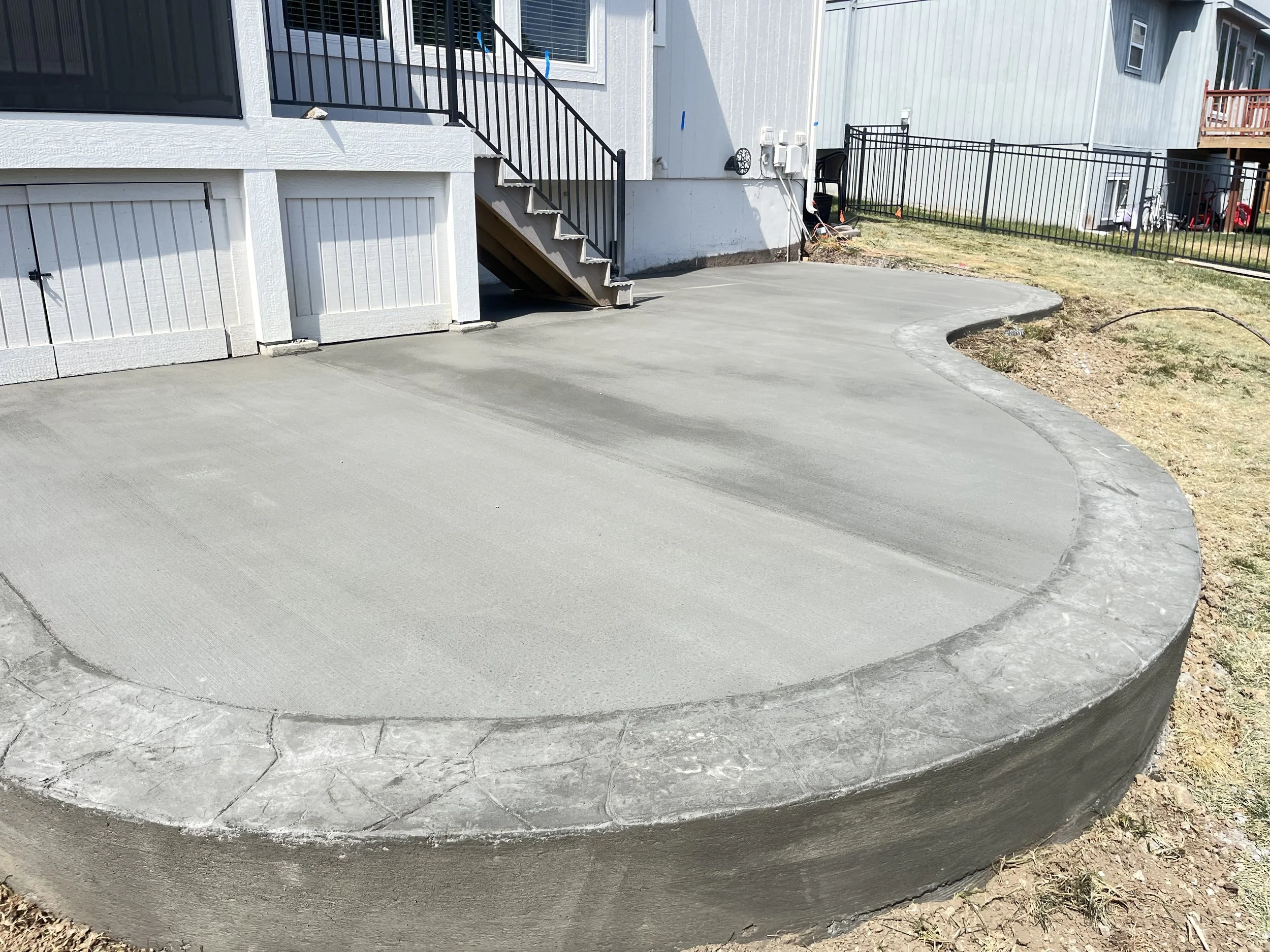Freshly poured concrete patio in front of a house with stairs and a sliding door.