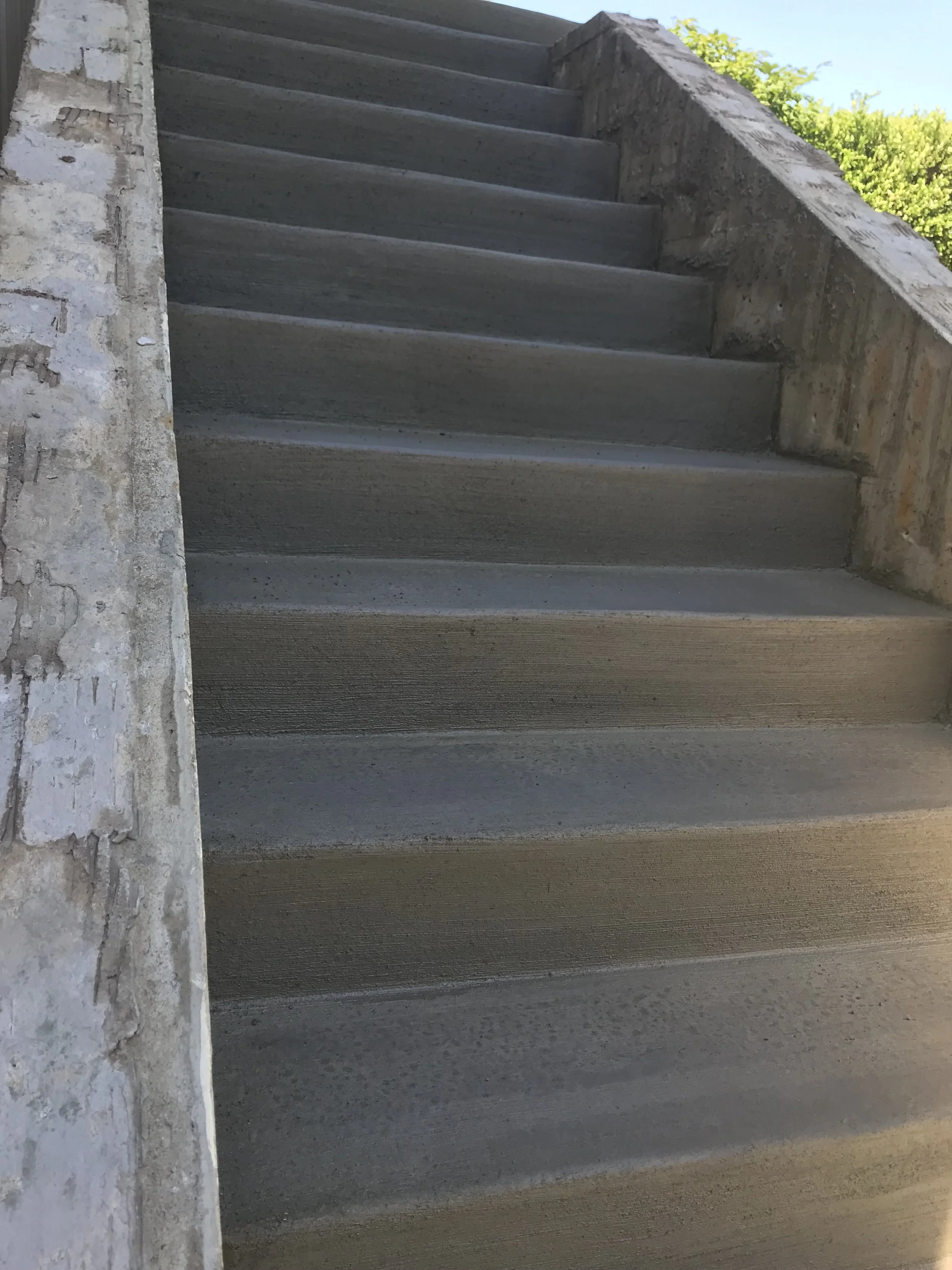 Concrete stairs with a brick wall on the side and some greenery in the background.
