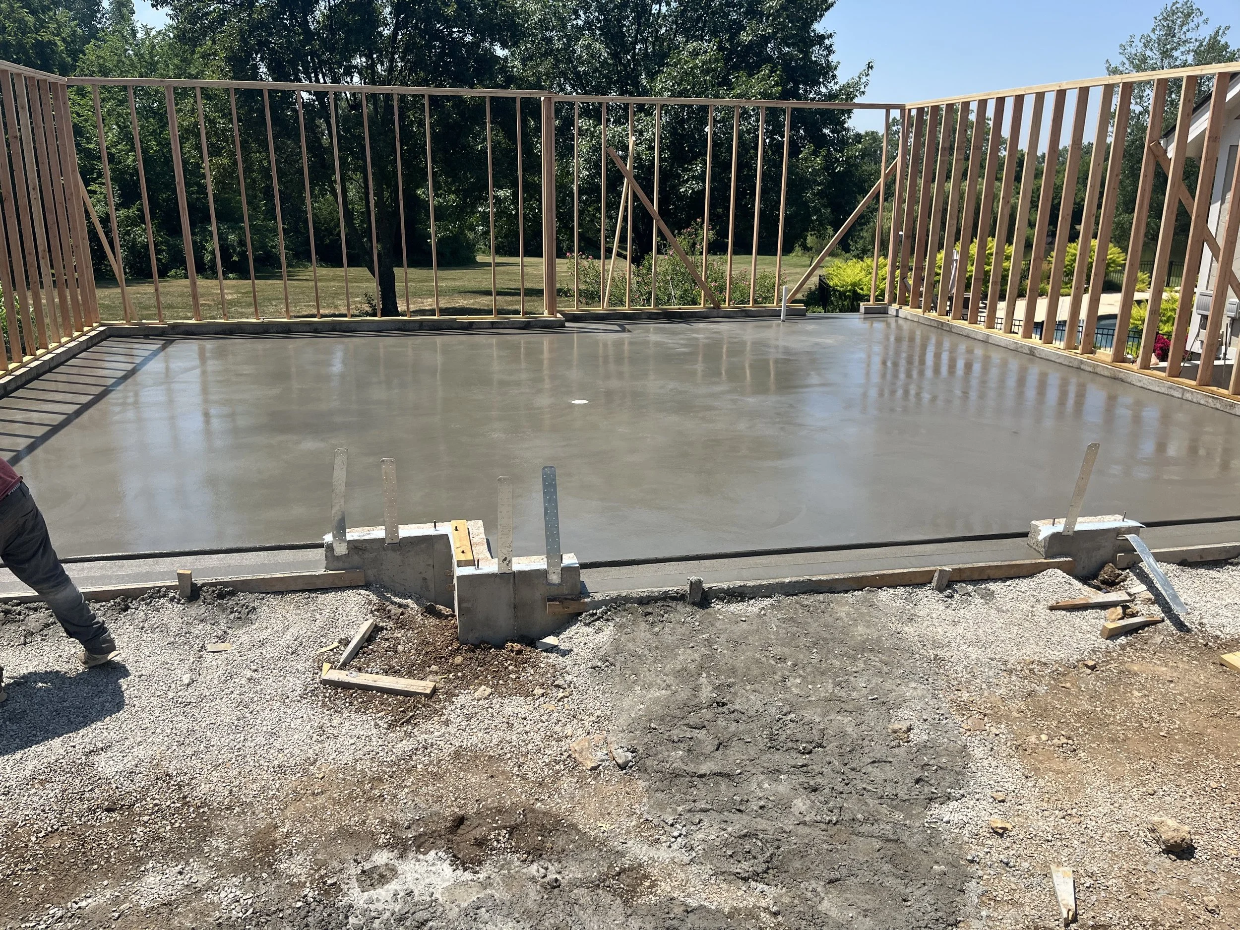 A new concrete patio being poured and smoothed, with wooden framing around it and a backyard with trees in the background.