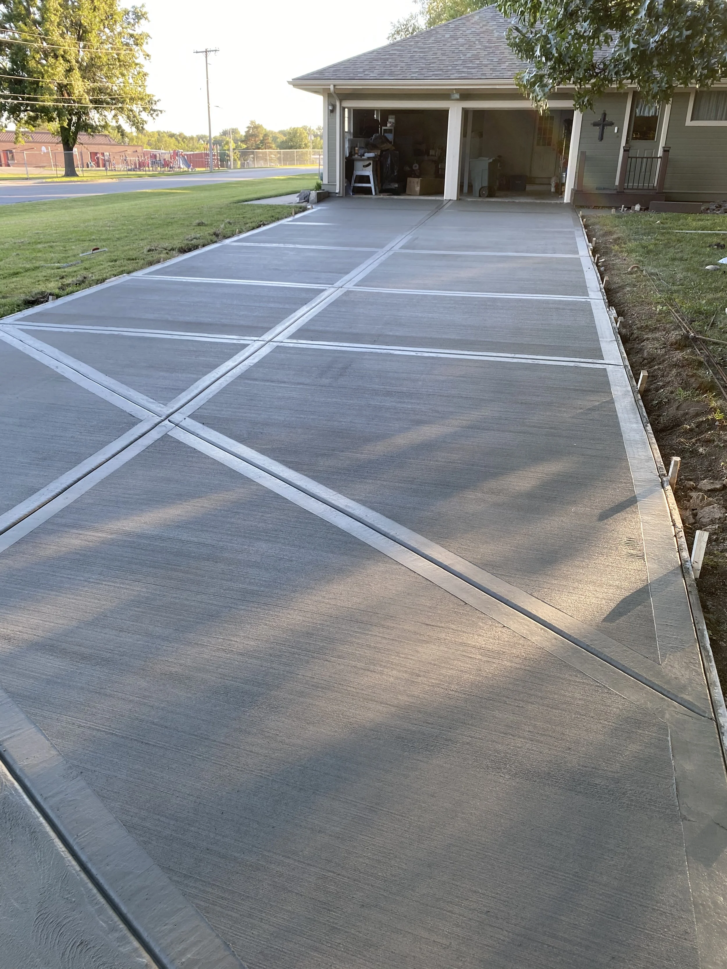 Newly constructed concrete driveway leading to an open garage on a house with some tools and storage inside.