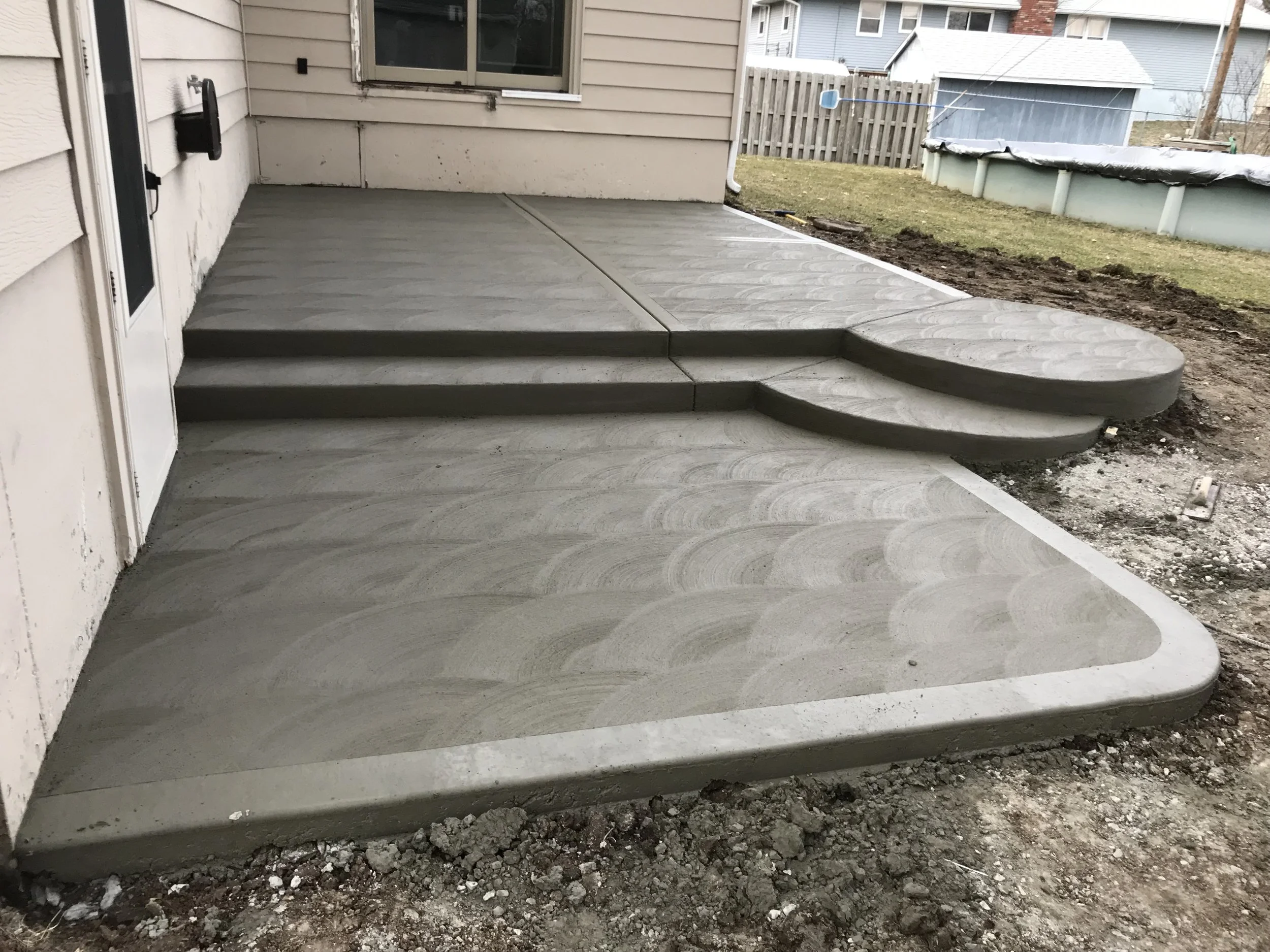 Newly constructed concrete porch and steps outside a house, with a grassy yard and portable pool in the background.