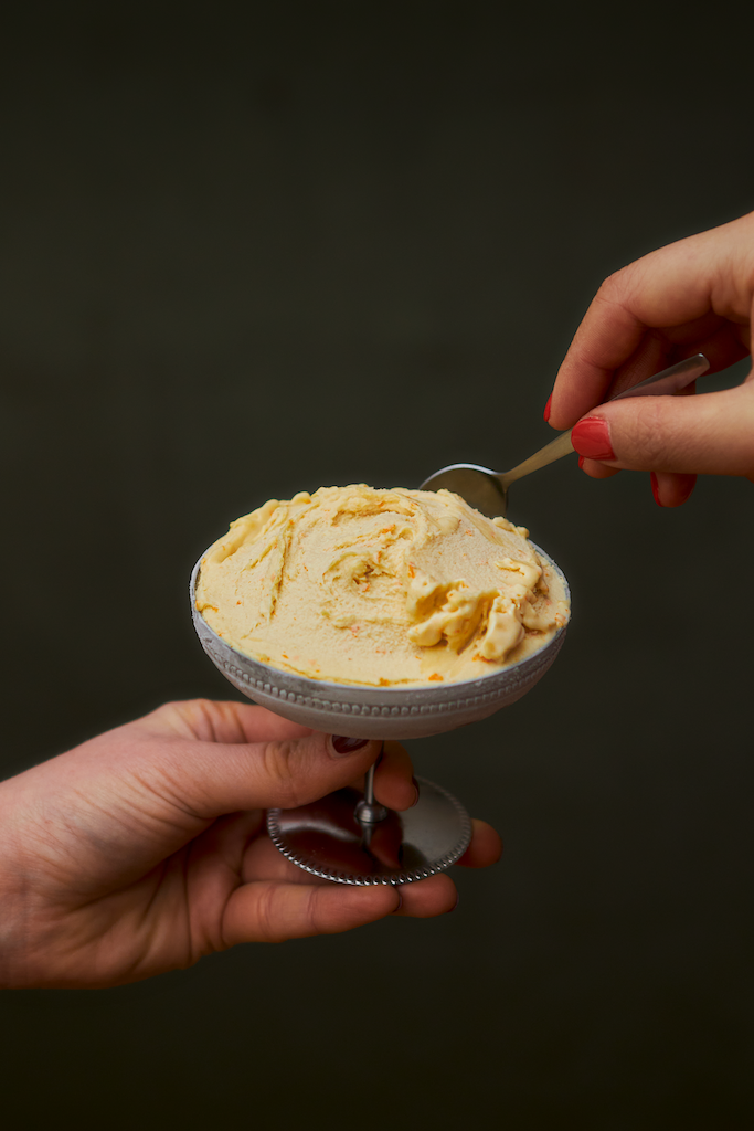 Deux mains tiennent une coupe contenant une crème glacée à la vanille, l'une la soutenant et l'autre utilisant une cuillère pour la manger.