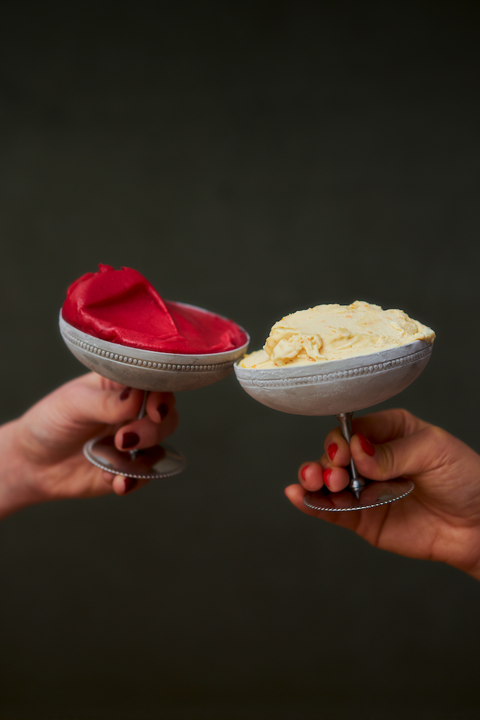 Deux coupes de glaces en inox saveur framboise et vanille tenues par deux mains pour trinquer