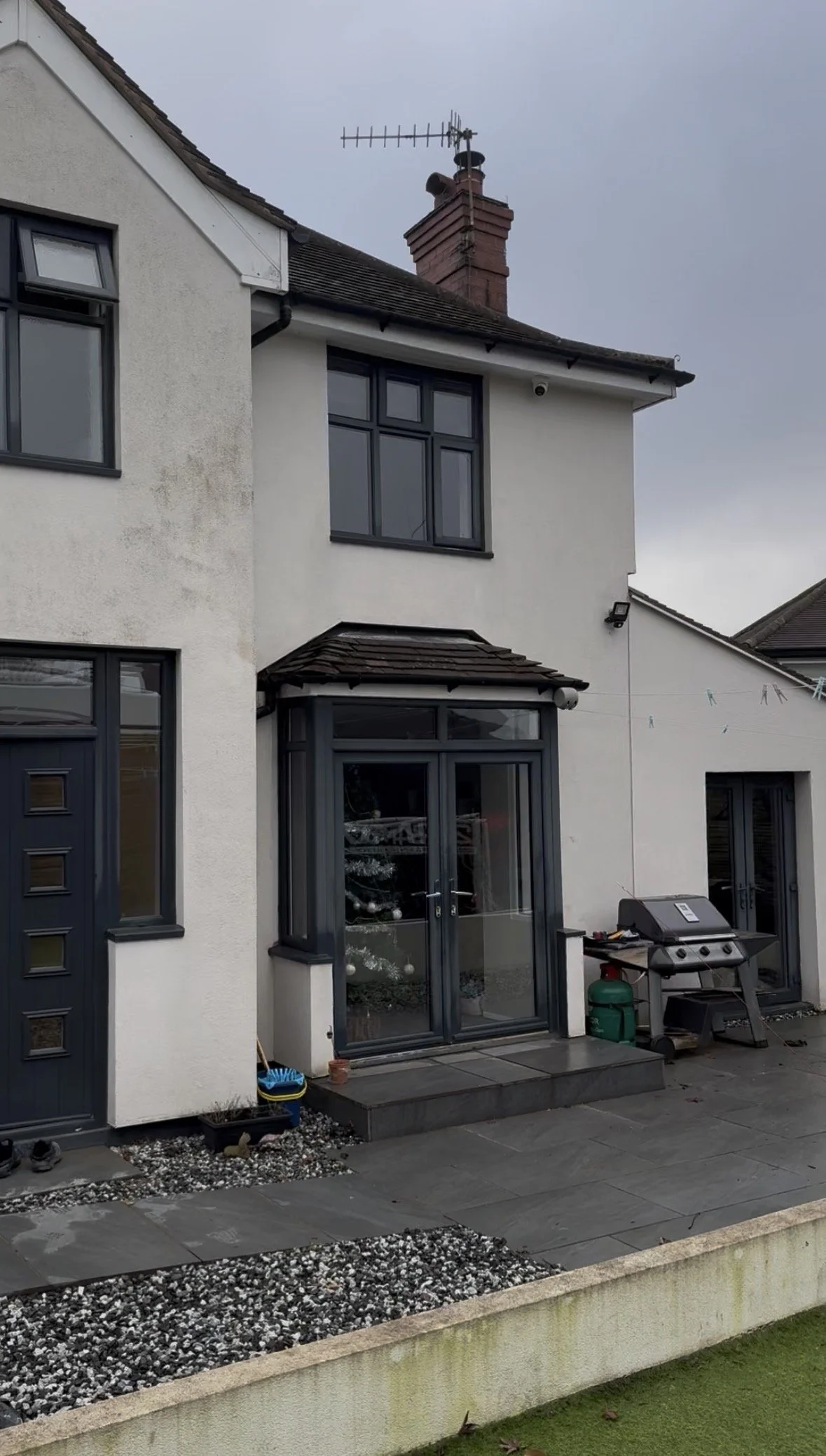 Backyard of a two-story house with a patio, barbecue grill, and Christmas decorations visible through a glass door.