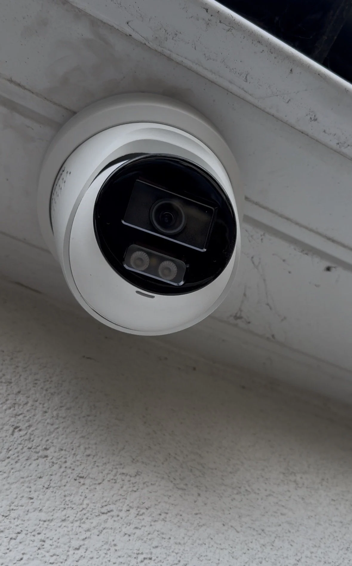 Security camera mounted on a white wall near a window.