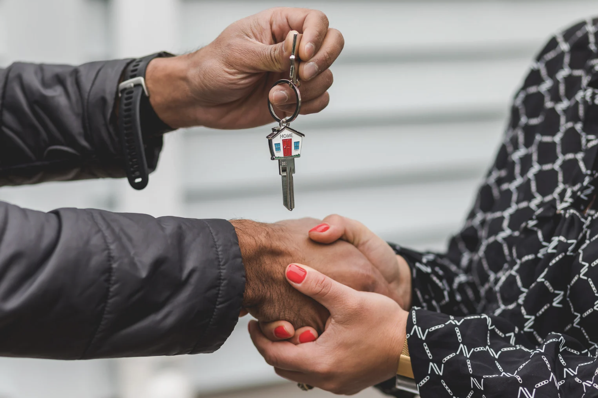 Person handing over keychain with house-shaped key to another person, symbolizing a property transaction.