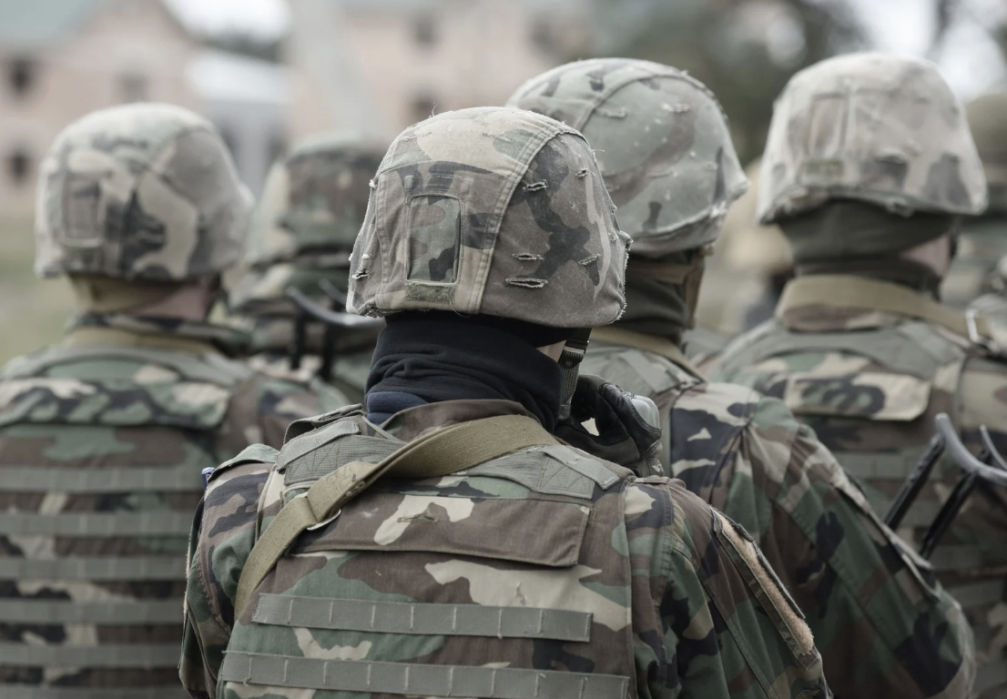 A group of soldiers in camouflage uniforms and helmets standing together outdoors.