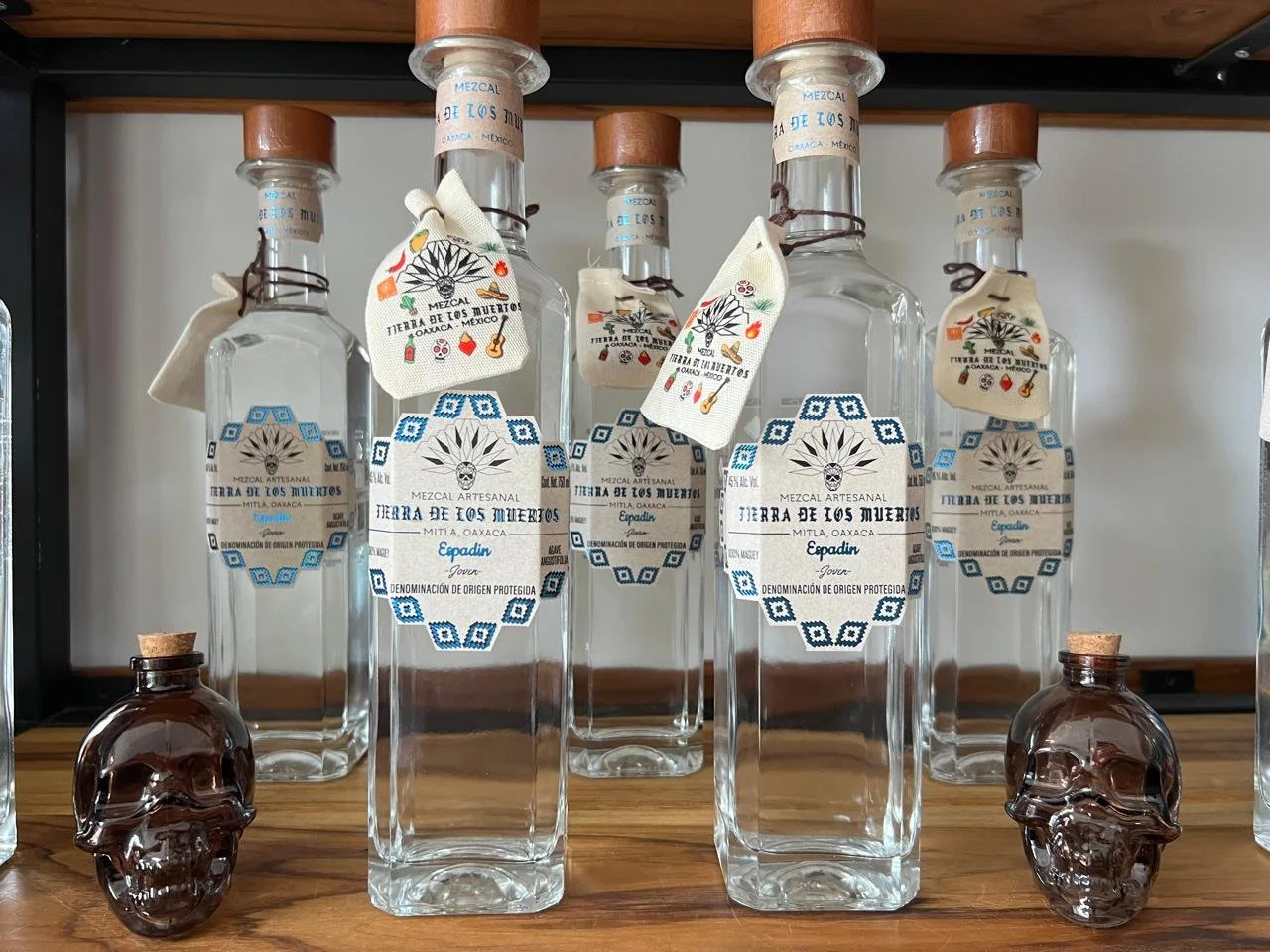A collection of tequila bottles, some with tags and two small skull-shaped bottles, displayed on a wooden surface.