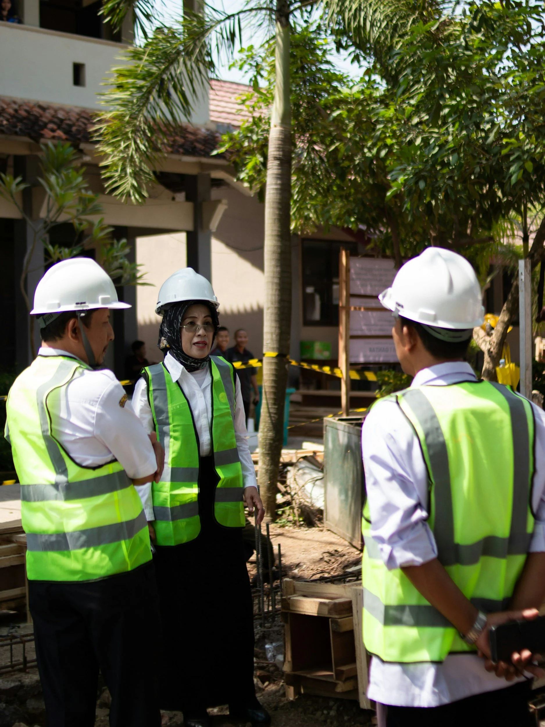 Three Inspectors having a discussion about a property inspection on a construction site with trees and building in the background.