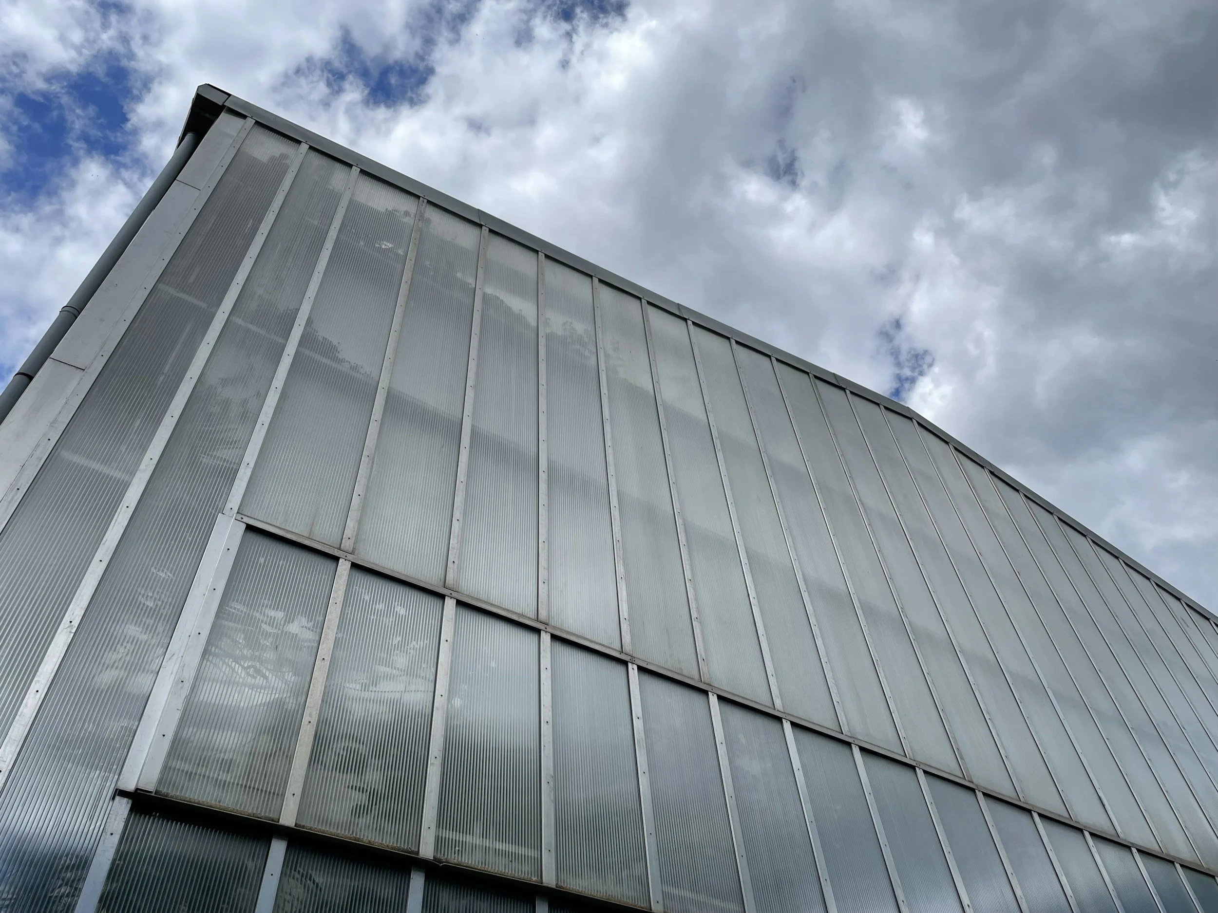 Photo of a modern building with metallic panels, taken from a low angle pointing up towards a cloudy sky.