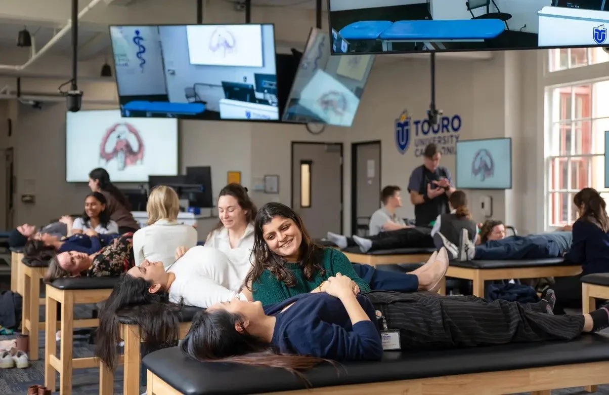 Dr Smriti Singh, founder and health provider at Trailhead Wellness Medicine, working with a patient providing care. Patient is lying on medical tables and smiling, with the medical professional and multiple monitors in the background.
