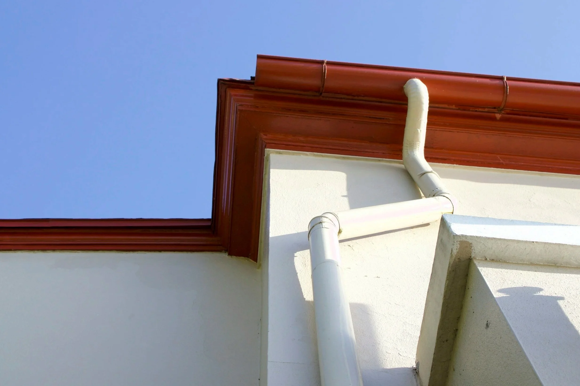 Close-up of the corner of a building with focusing on the functioning gutter drainage system against a blue sky.