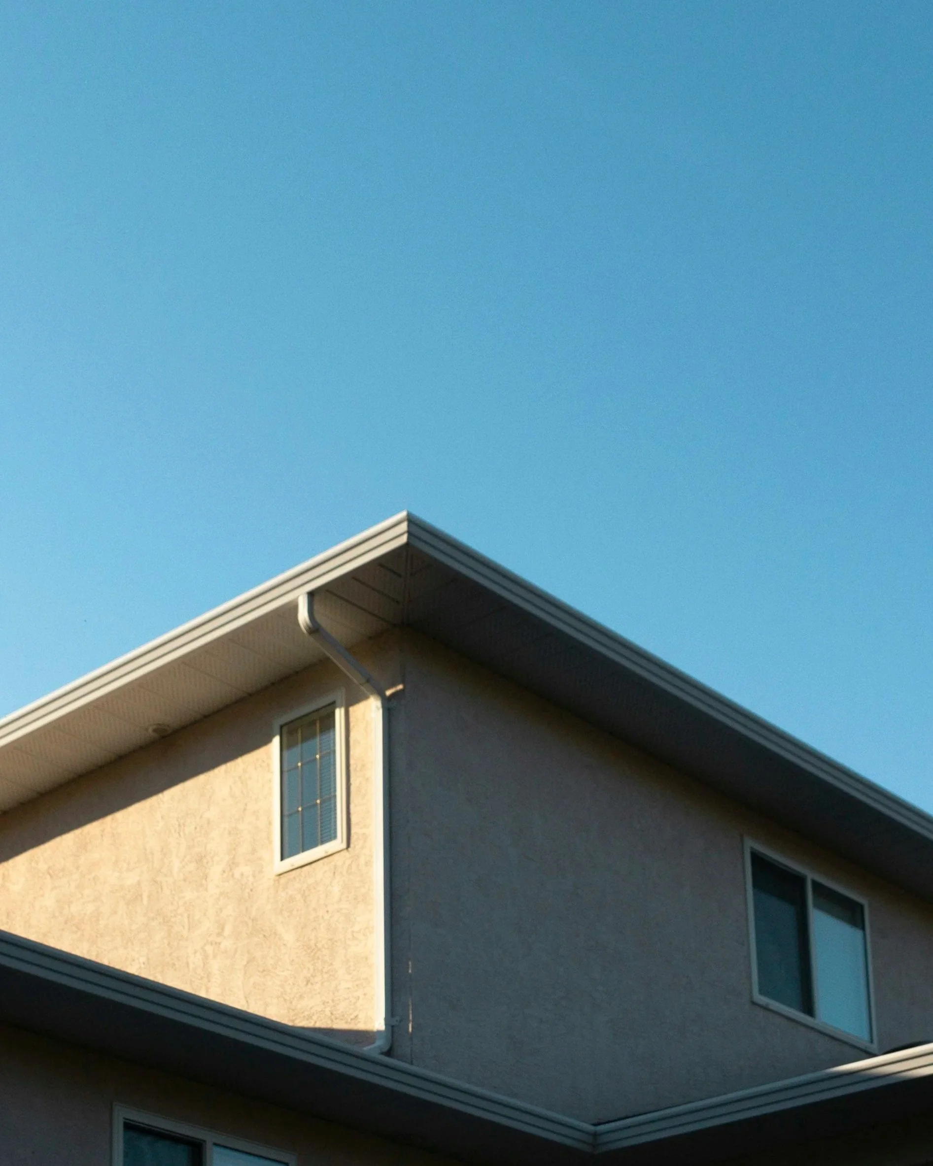 Part of a beige house with two streak-free windows and debris-free gutters.