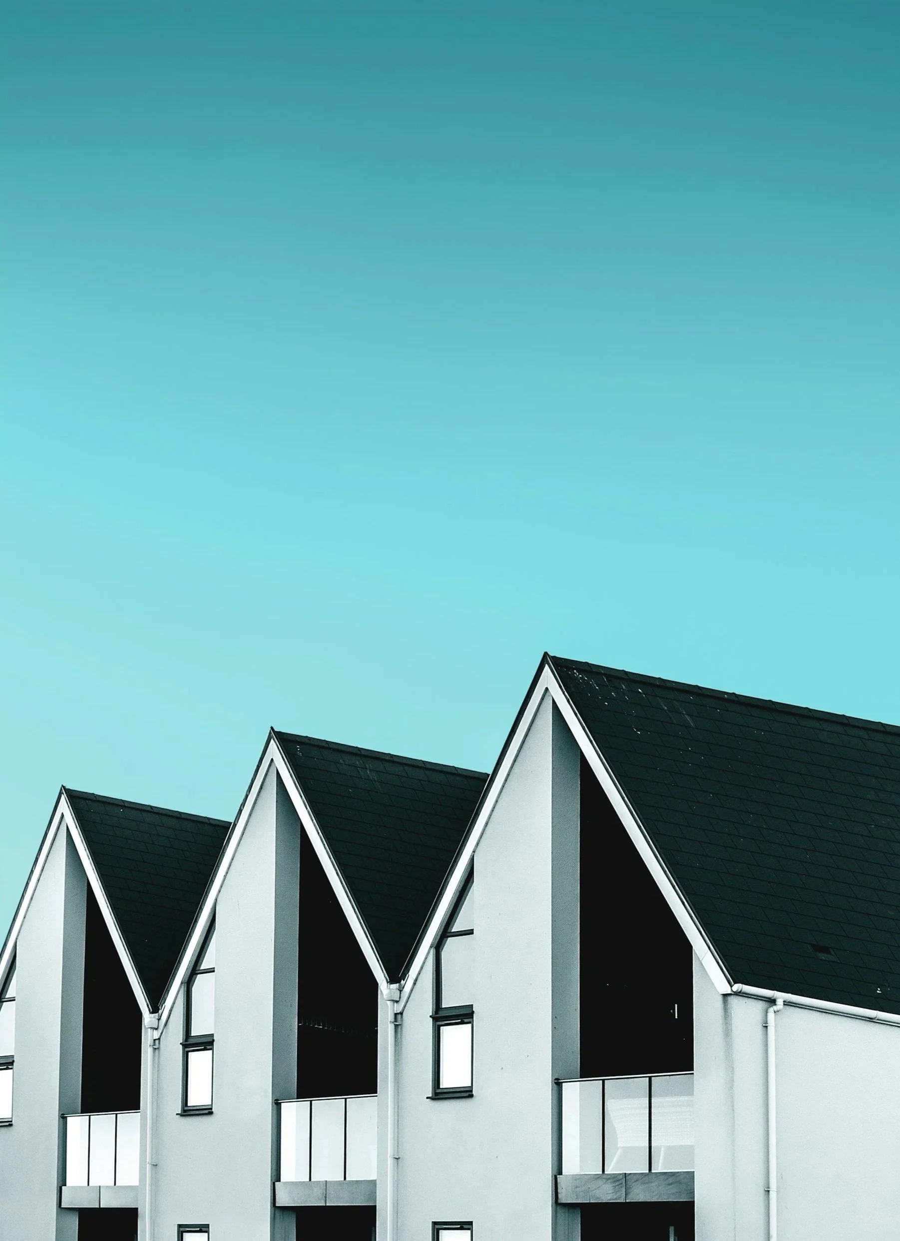 Modern commercial buildings with steep black roofs, clean windows and clear gutters, under a clear blue sky.