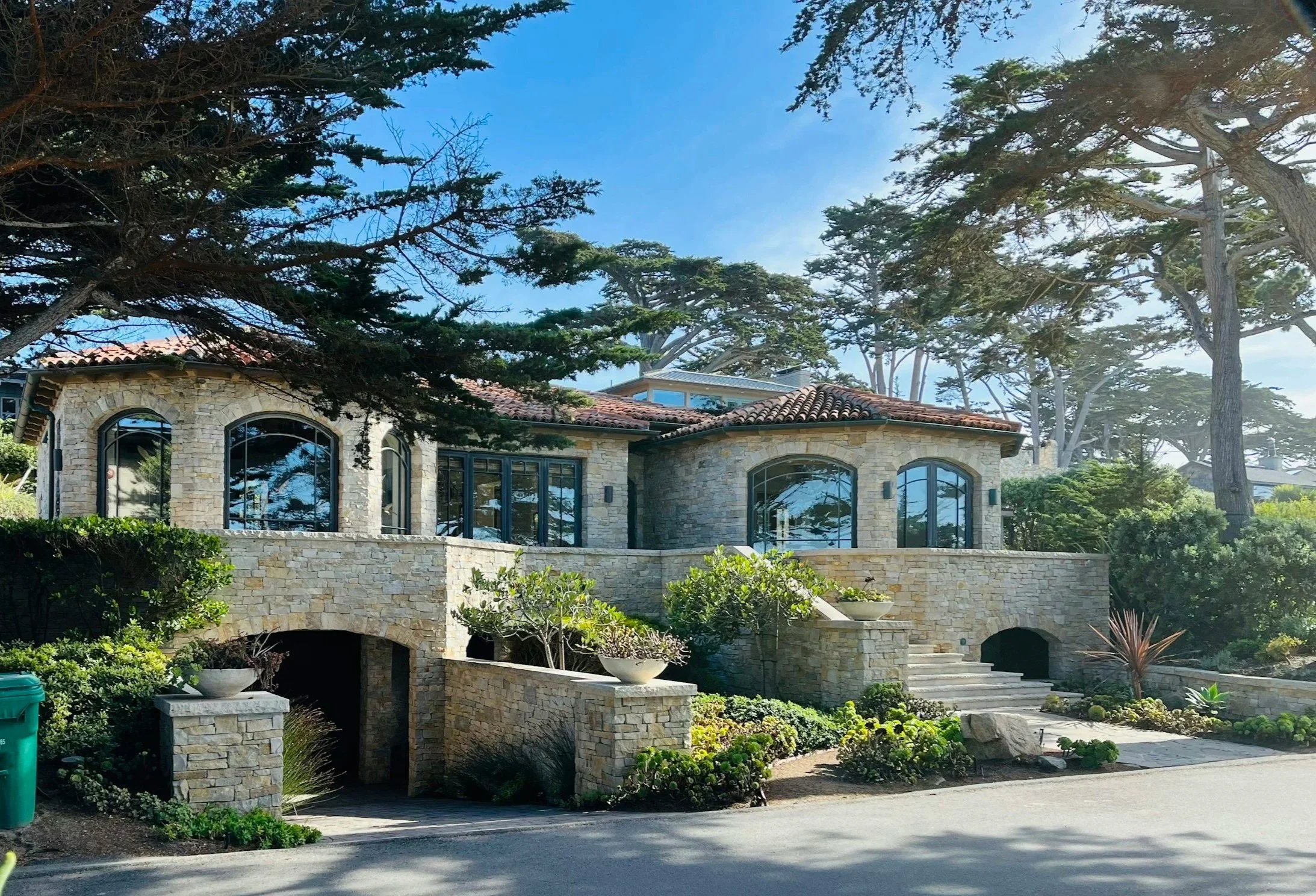 Large house near the coast, several immaculately cleaned arched windows reflecting the surrounding trees and landscaped garden.