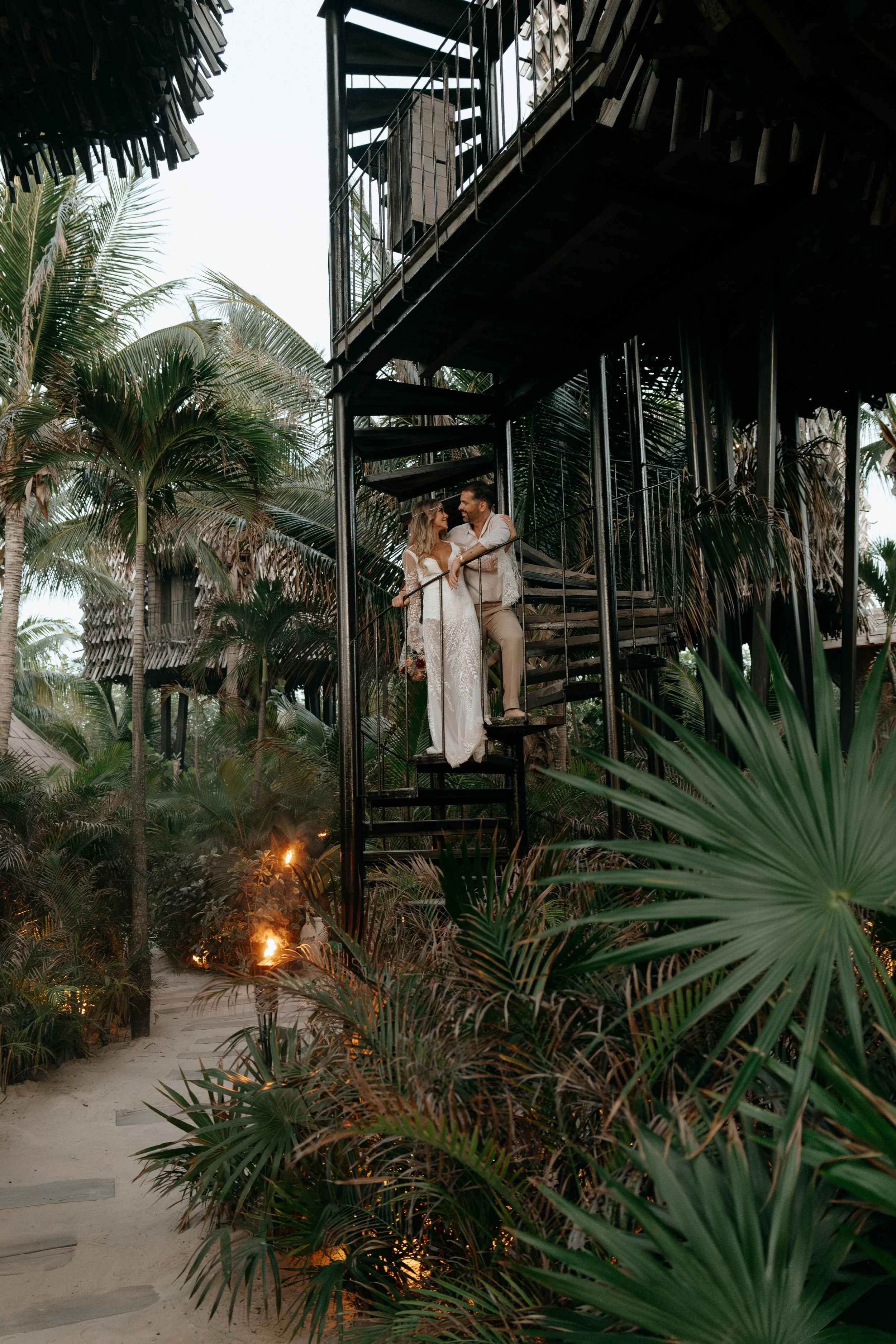 Couple standing on a spiral staircase surrounded by tropical greenery at a Holbox wedding venue.