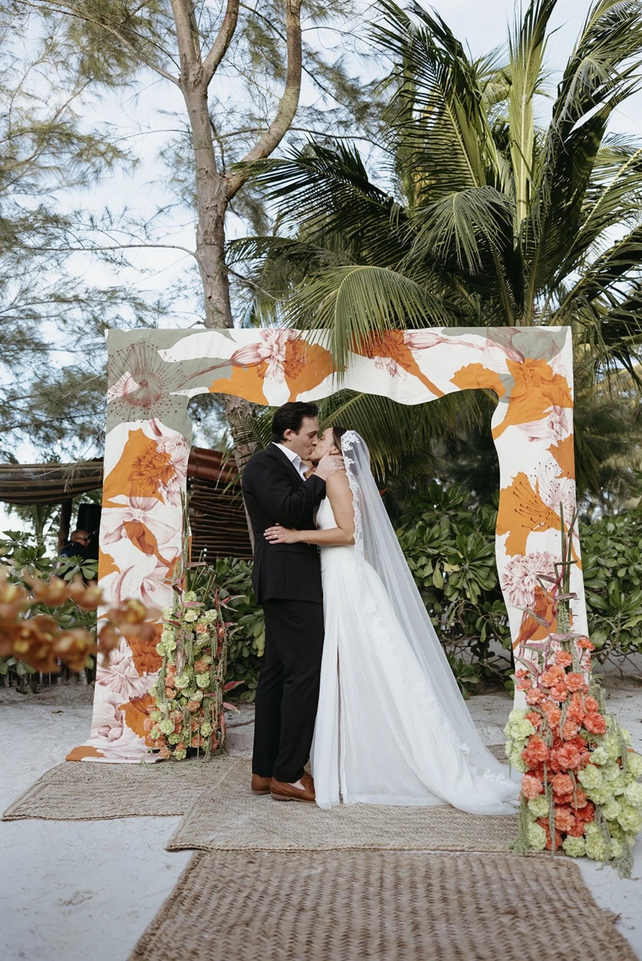 Bride and groom kissing beneath a floral arch during an outdoor wedding ceremony in Holbox.