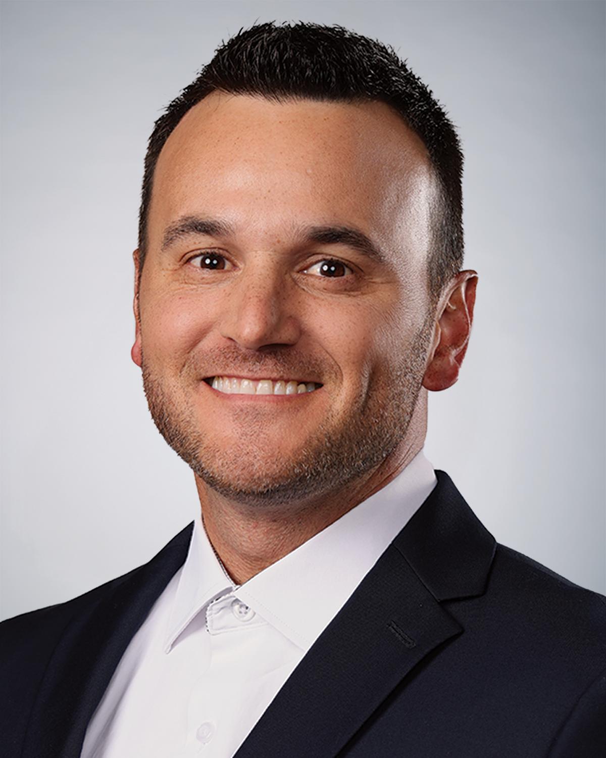 Headshot of a smiling man in a suit and white shirt.