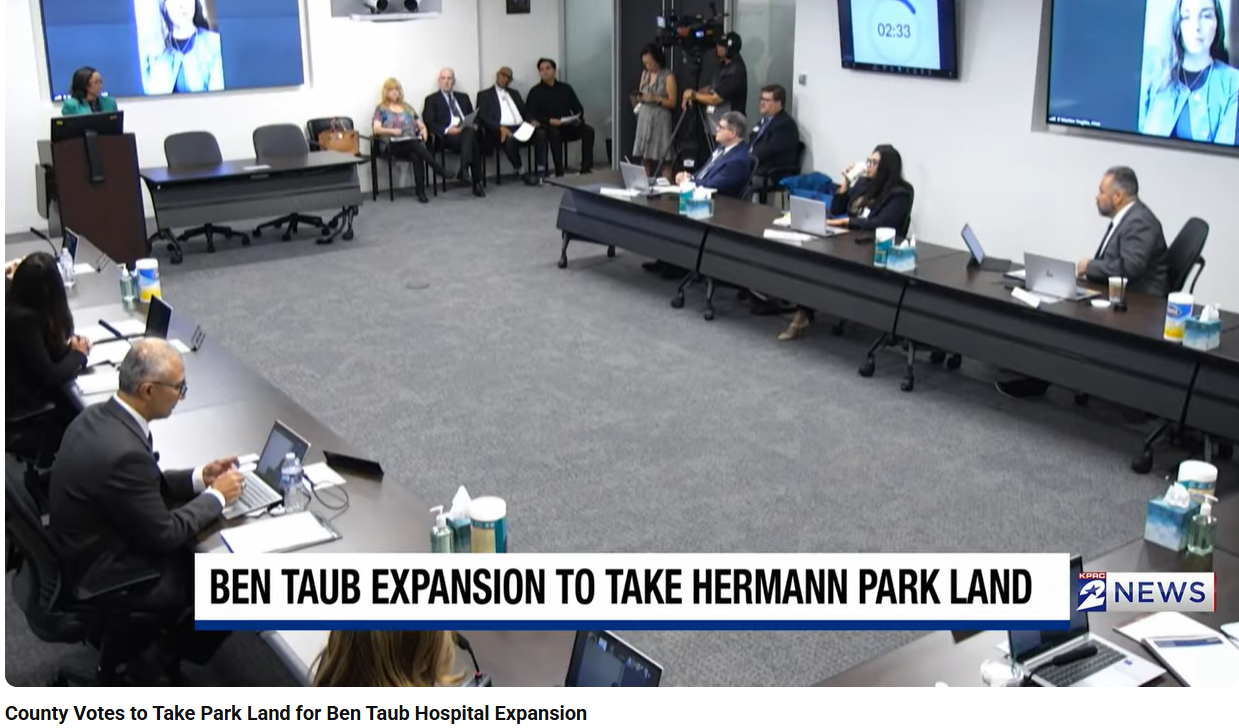 A conference room with people seated at long tables, some working on laptops, during a meeting discussing land expansion.