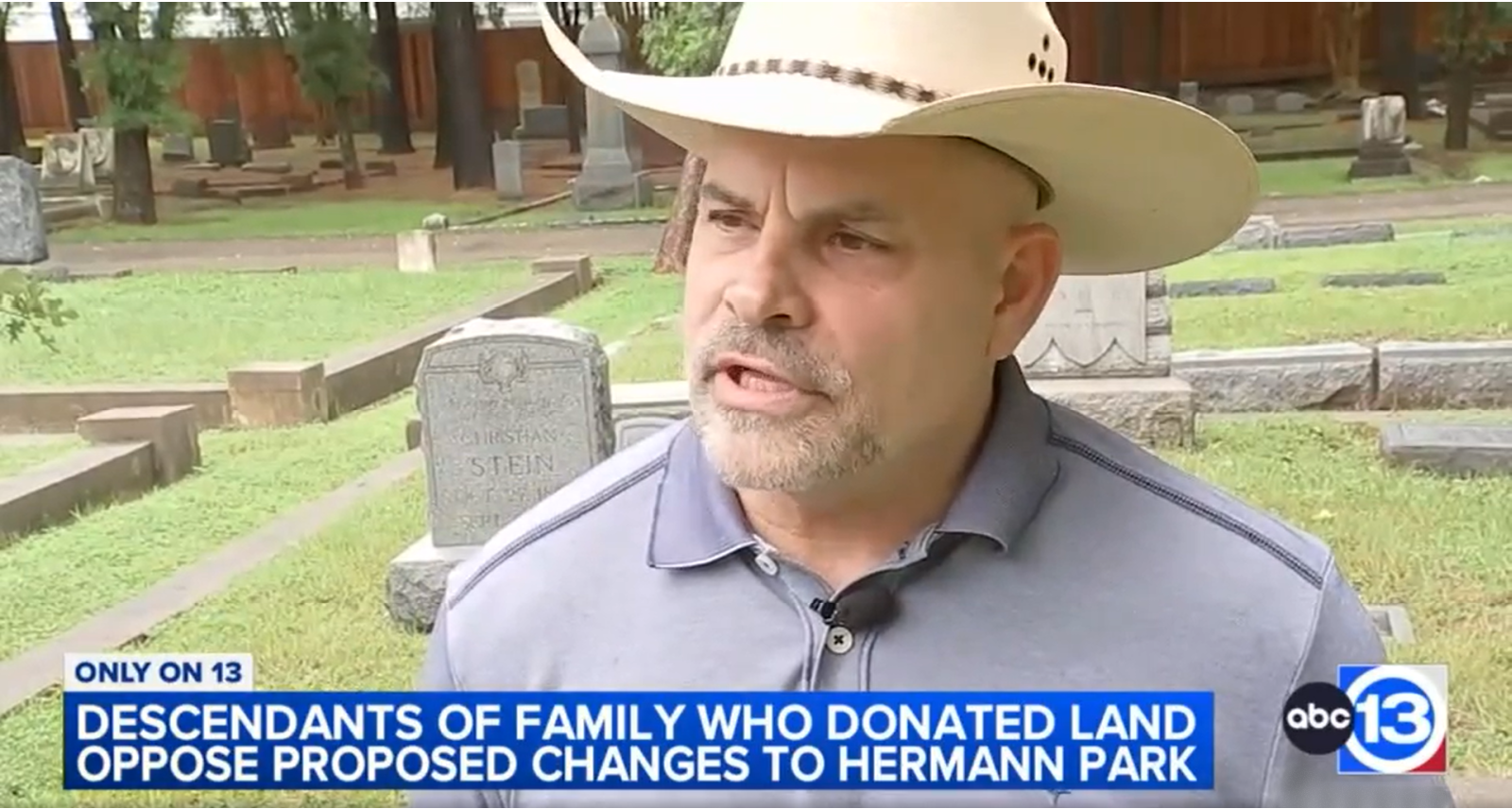 A man wearing a cowboy hat and a gray shirt speaking during a news interview in a cemetery, with tombstones visible in the background. The news caption discusses descendants of land donors opposing changes to Hermann Park.