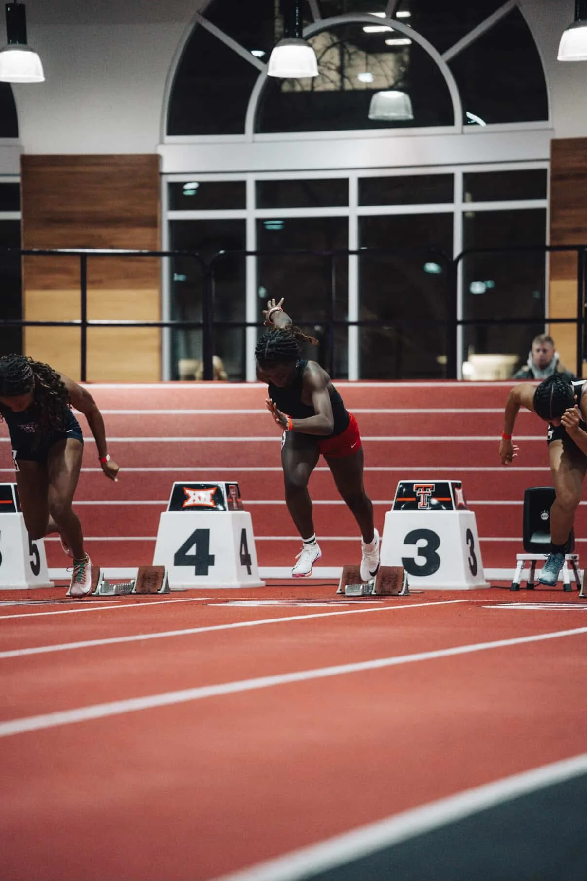 Track athletes at the starting blocks during an indoor track race in a sports facility.