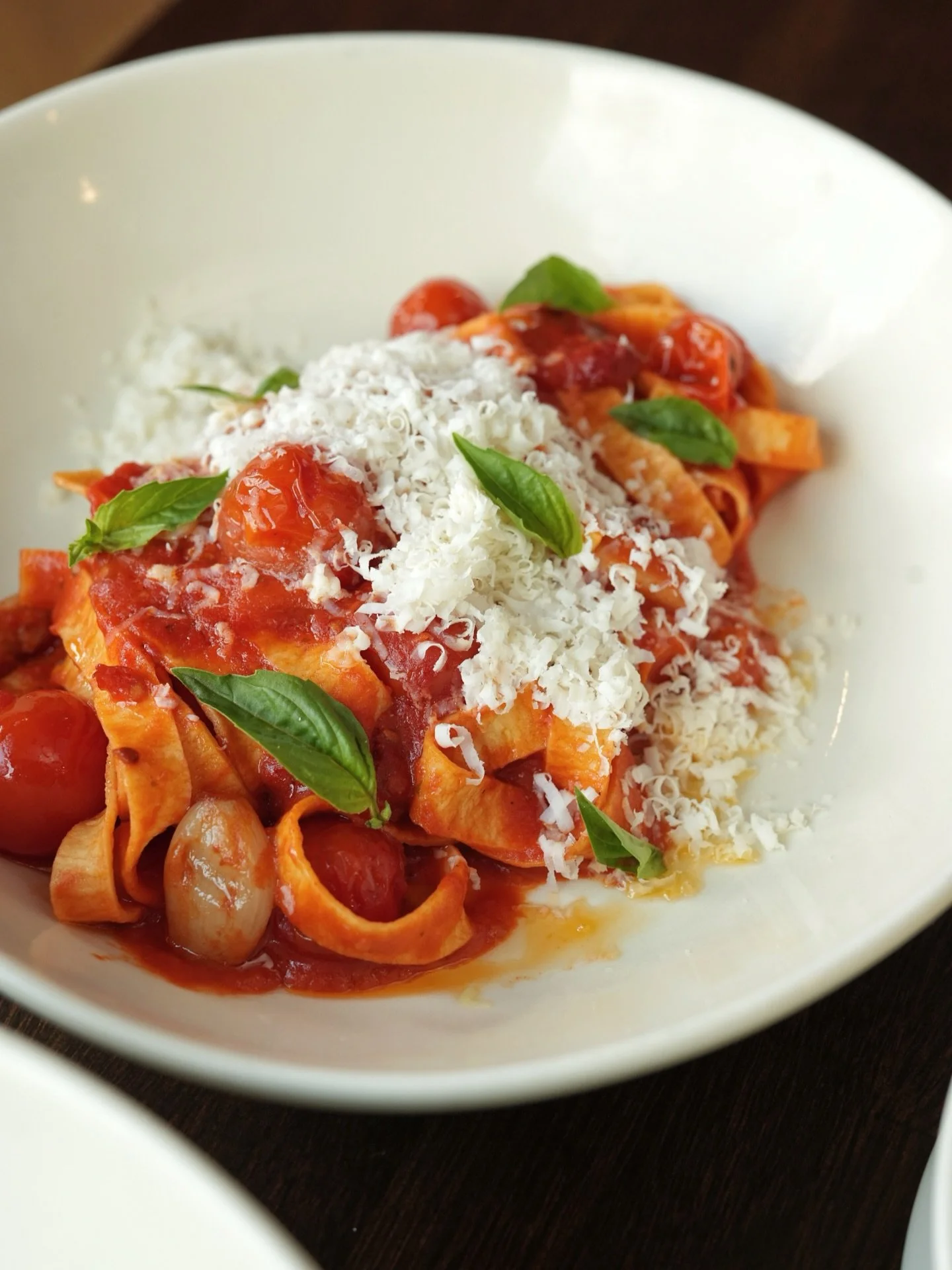 Red ribbons of pasta. Golden garlic. Tomatoes bursting with sweetness. A snow of ricotta salata. 

Tagliolini Pomodoro. Order it once, crave it forever.