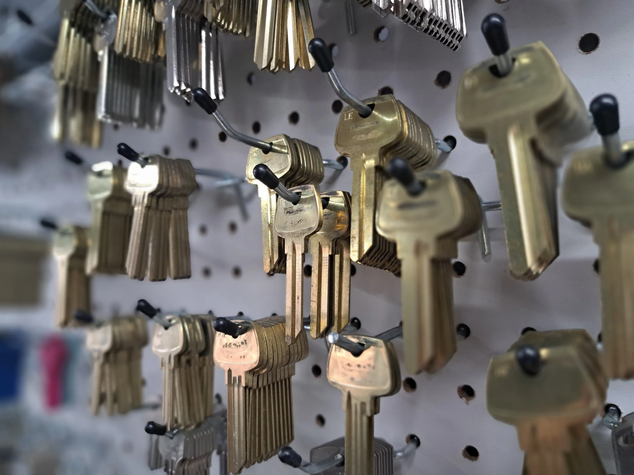 A display of multiple brass keys hanging on hooks against a pegboard wall.