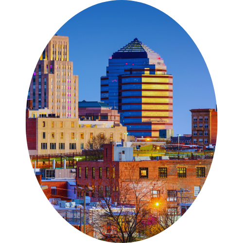 City skyline with a prominent modern, stepped skyscraper during dusk, surrounded by other buildings and trees.