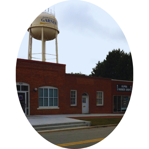 A water tower labeled 'GARNER' above a brick building with barber shop and storefronts on a cloudy day.