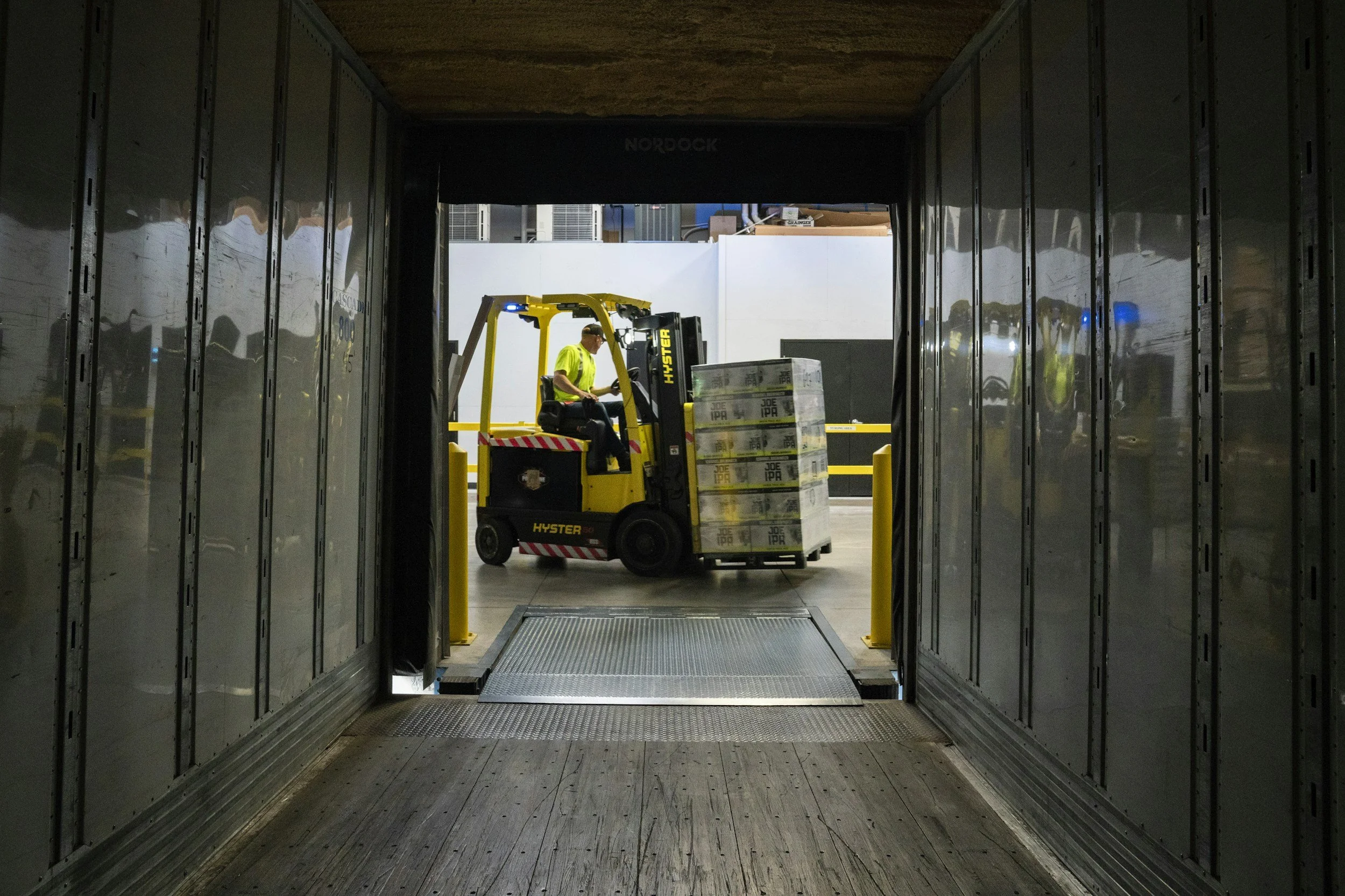 Forklift moving palletized boxes at the open end of a freight truck.