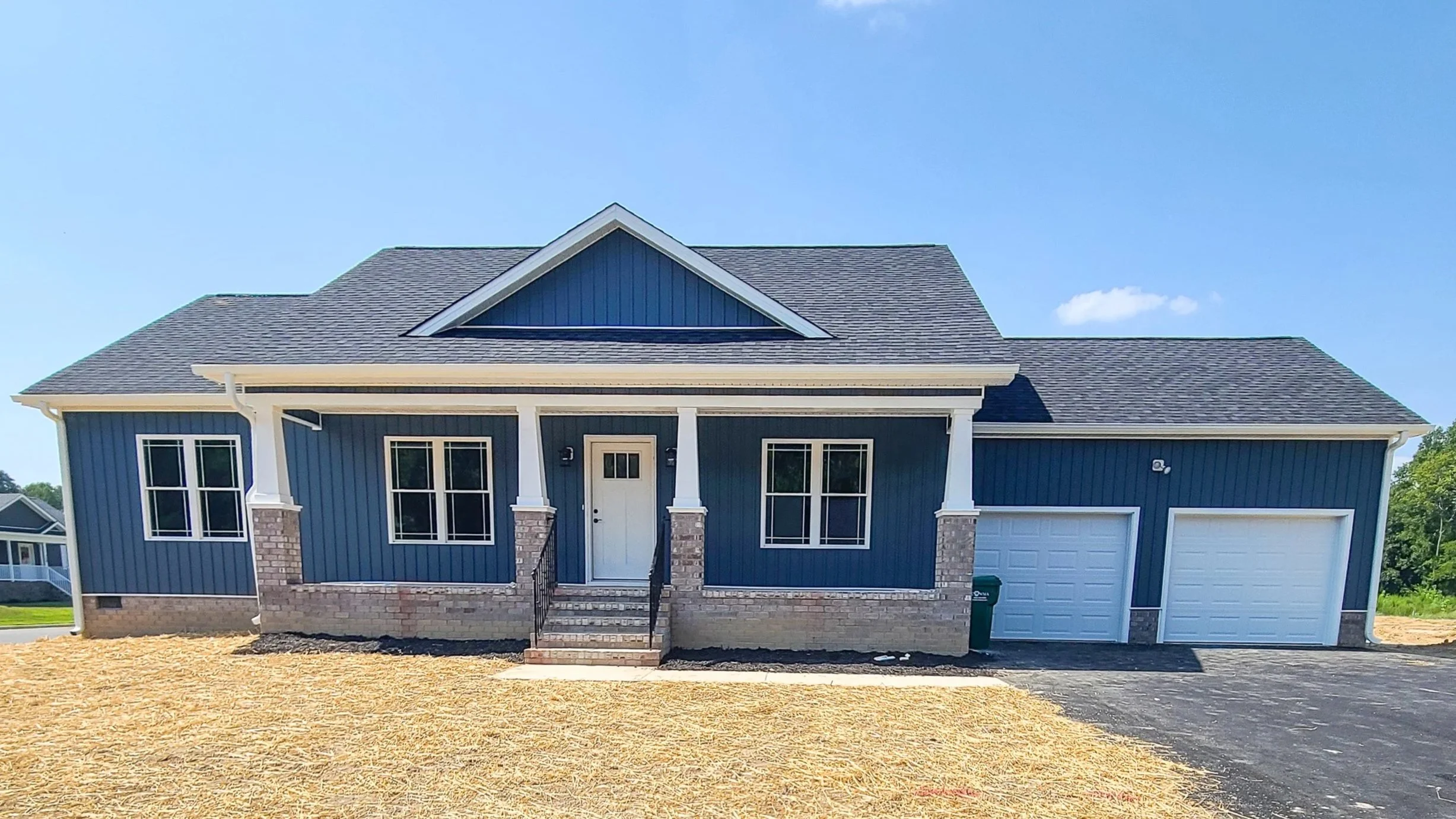 New blue house with white trim, front porch, and two garage doors, under a clear blue sky.