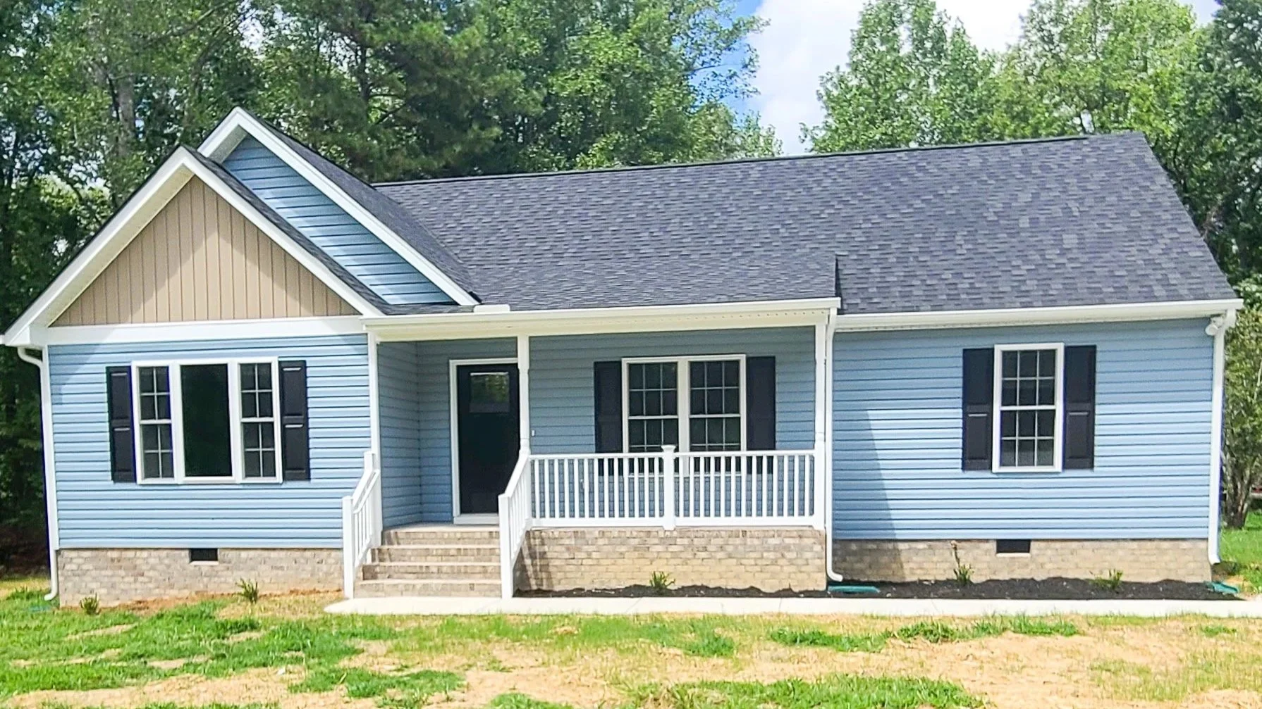 Light blue house with white trim, black shutters, and a dark gray roof, front porch with steps, surrounded by grass and trees.