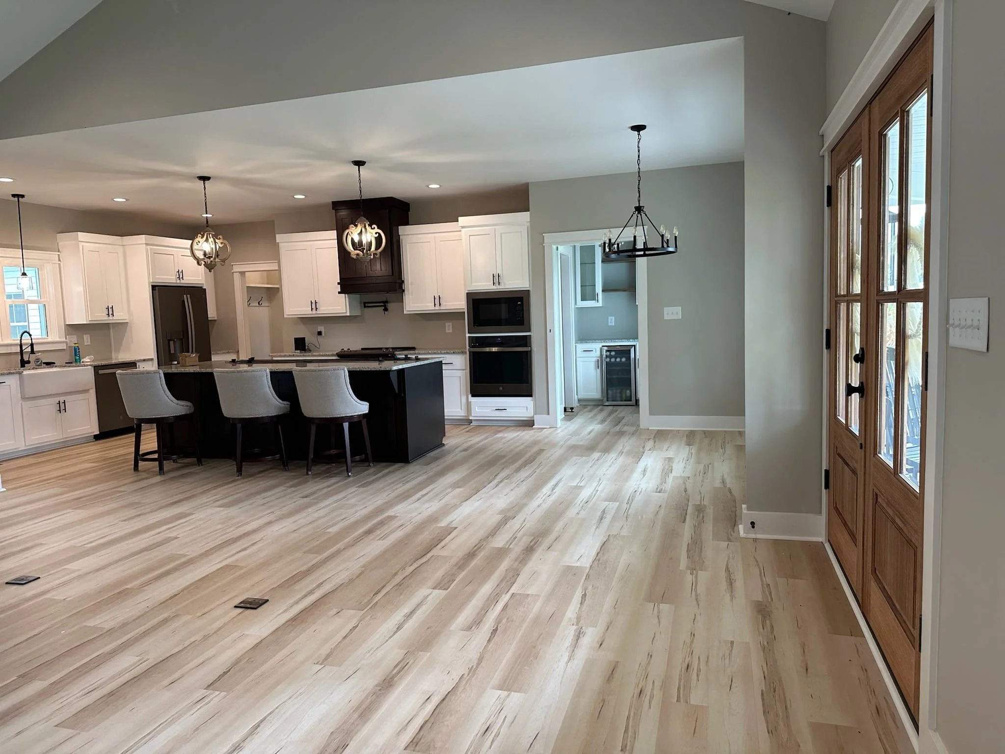 Spacious, modern kitchen with white cabinets, black accents, light wood flooring, and a dining area with a black chandelier. Features include a kitchen island with four barstools, stainless steel appliances, and a sliding door with glass panels.