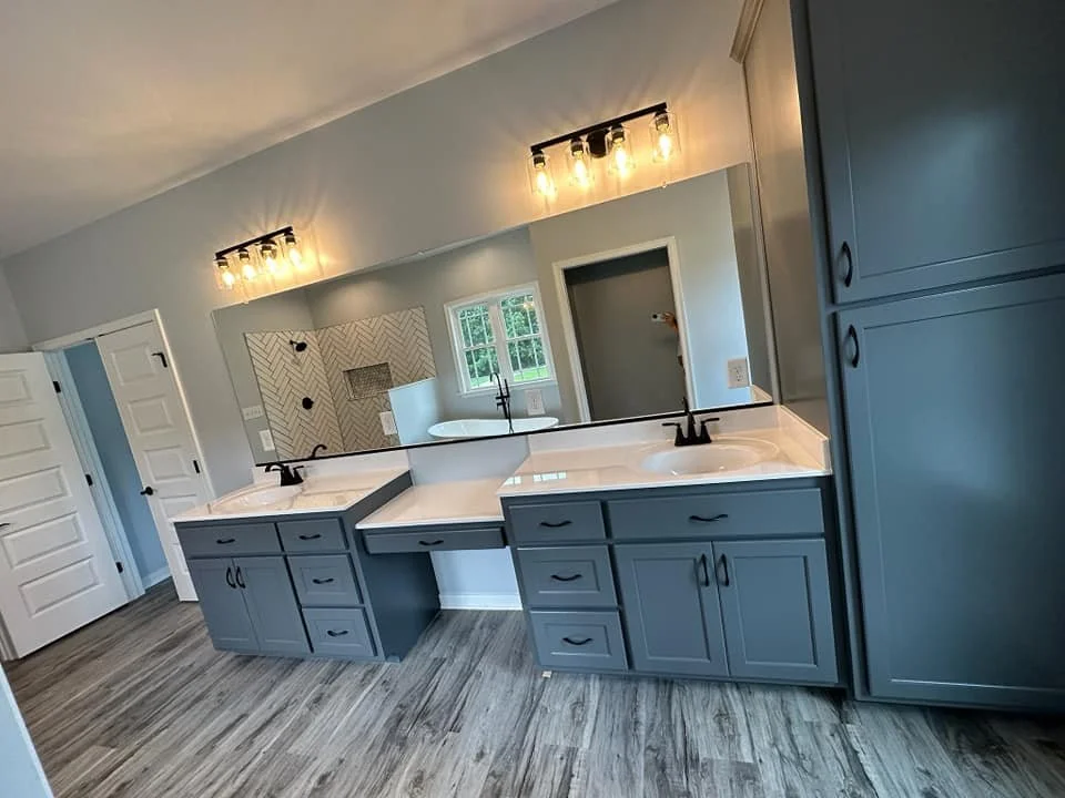 Modern bathroom with double vanity sinks, gray cabinets, a large mirror, and a walk-in shower in background.