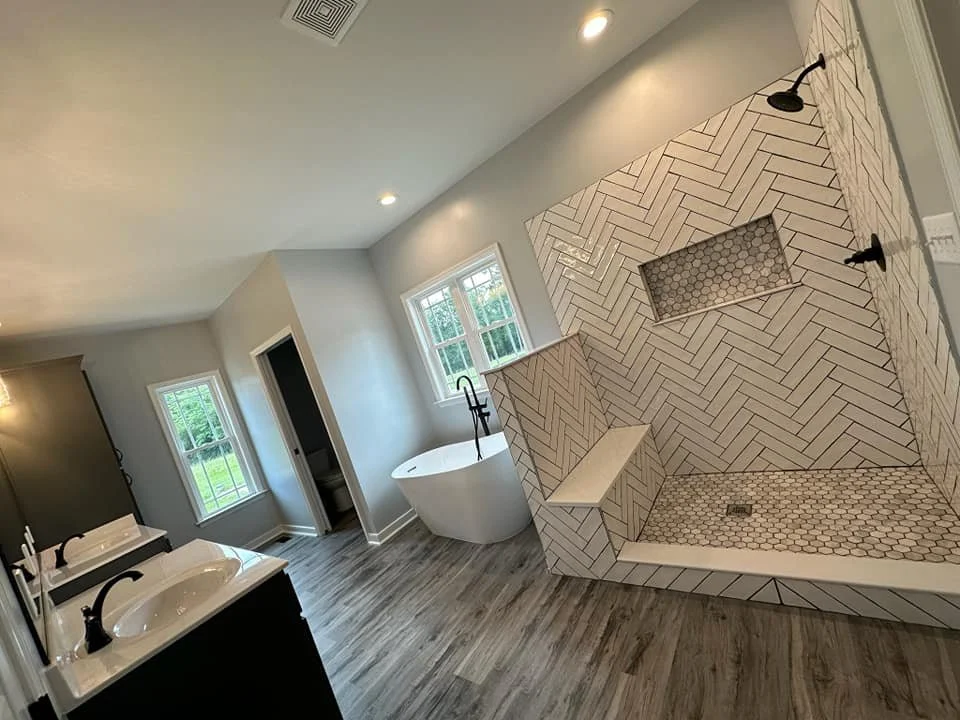 Modern bathroom with a free-standing bathtub near a window, a double sink vanity with black fixtures, and a large walk-in shower with white herringbone and honeycomb tiles.