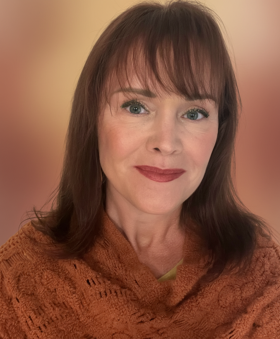 A woman with light skin, shoulder-length brown hair with bangs, wearing makeup with lipstick and eye makeup, smiling, wearing a rust-colored knitted sweater, against a blurred neutral background.
