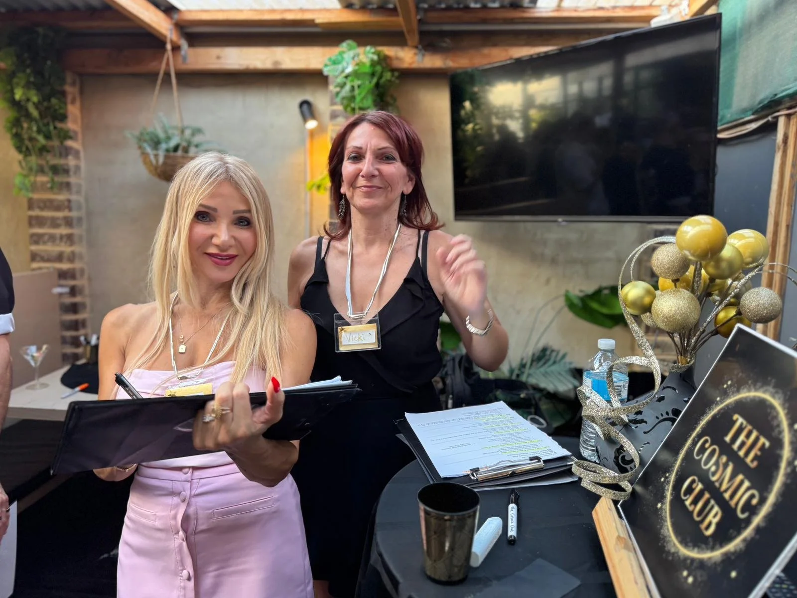 Group of five adults celebrating with drinks at a bar, raising their glasses in a toast, smiling, with warm lighting and bokeh lights in the background.