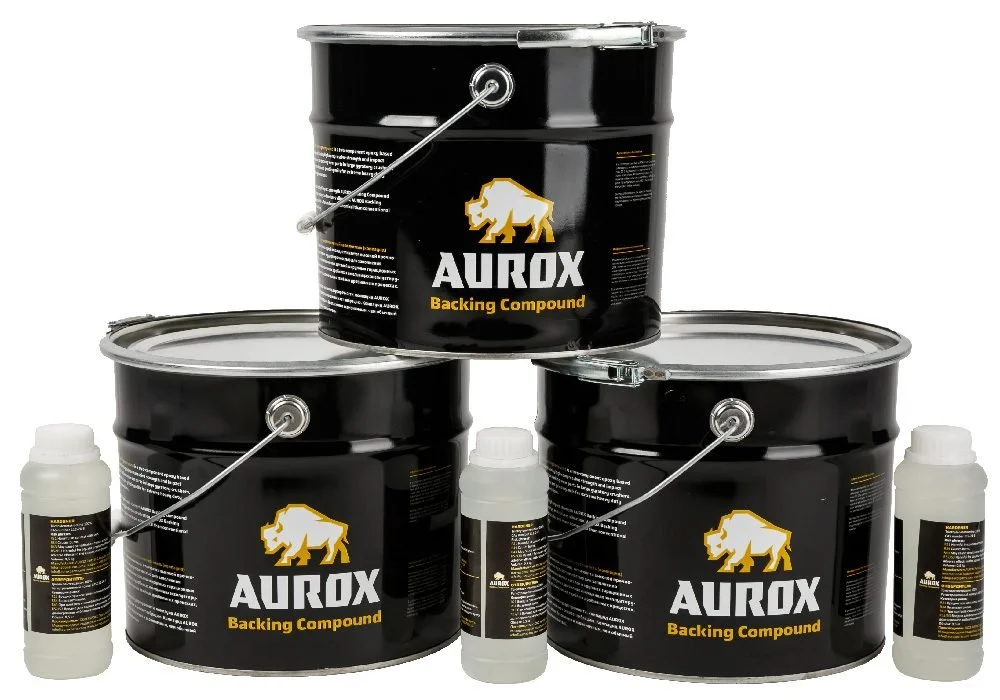 Kolme mustaa maalia sisältävää tamburiä, joissa on kultainen ja valkoinen leijona-logo ja teksti 'AUROX Backing Compound', kahdessa pieniä valkoisia pulloja.