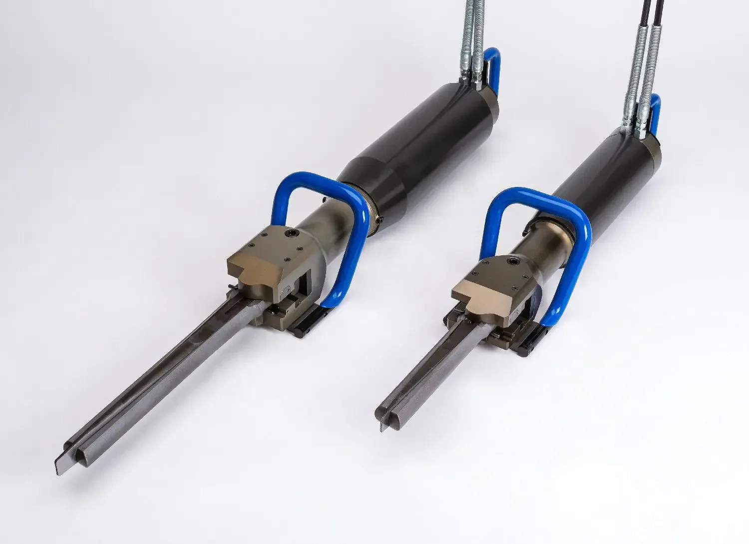 Kaksi teollisuusrobottia tai -työkalua, joissa on pitkä metallinen varsi ja tummat runko-osat, punaiset ja harmaat pelkät osat, sekä siniset kahvat.