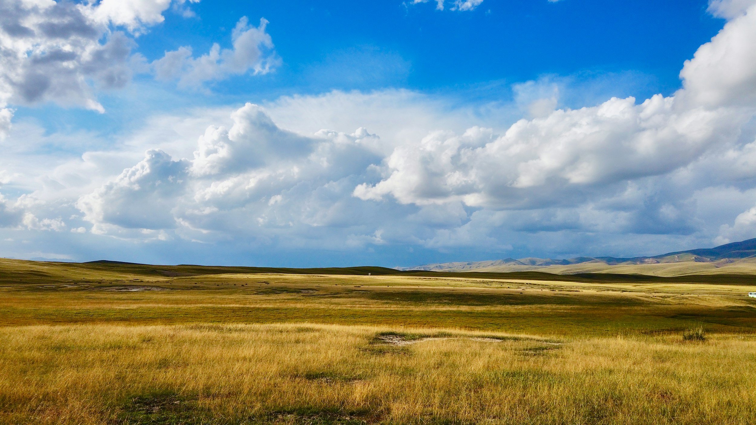 Wide view of open grassland with rolling hills and a partly cloudy sky.