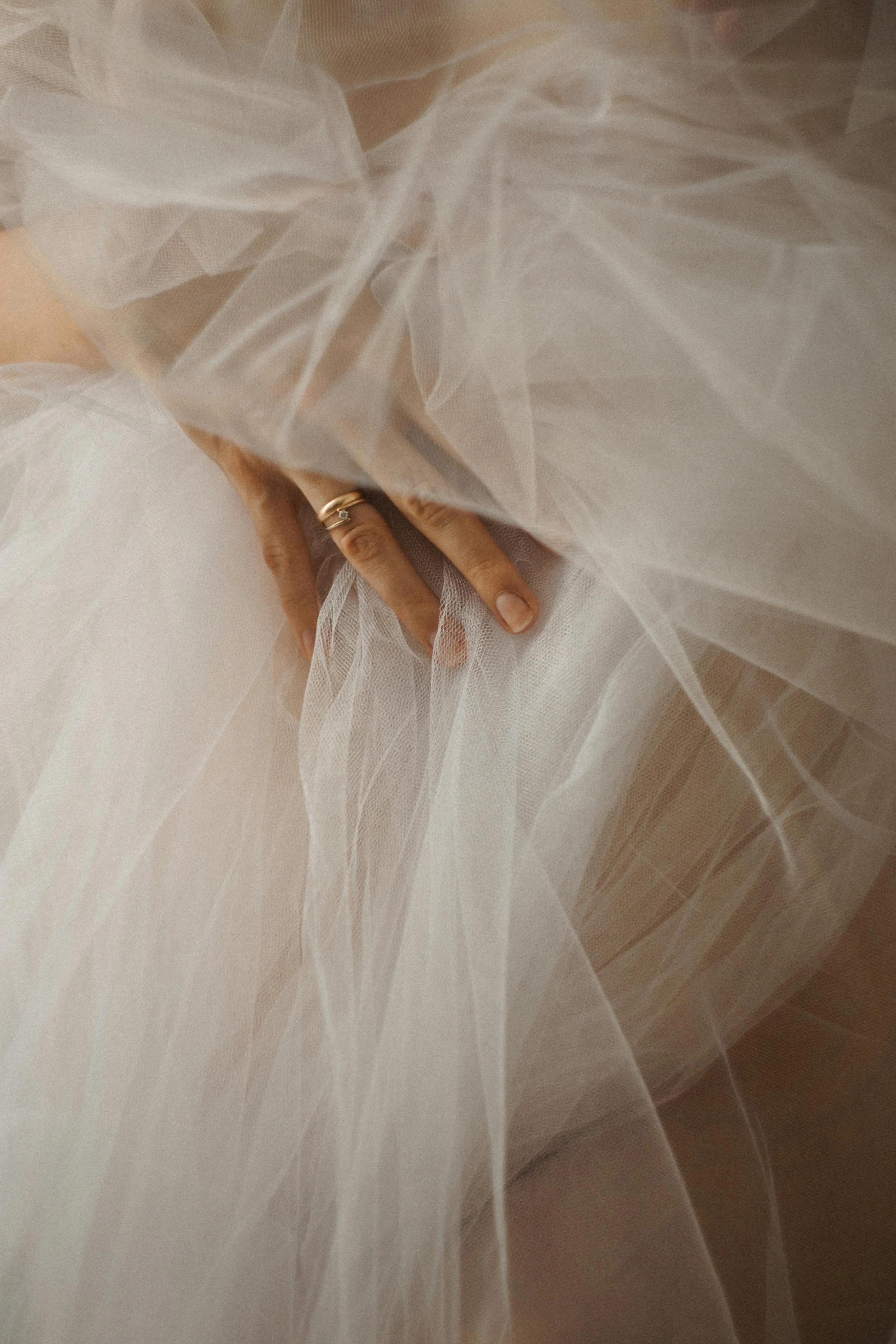 Close-up of a person adjusting a white tulle wedding dress, with hand and rings visible amid layers of fabric.