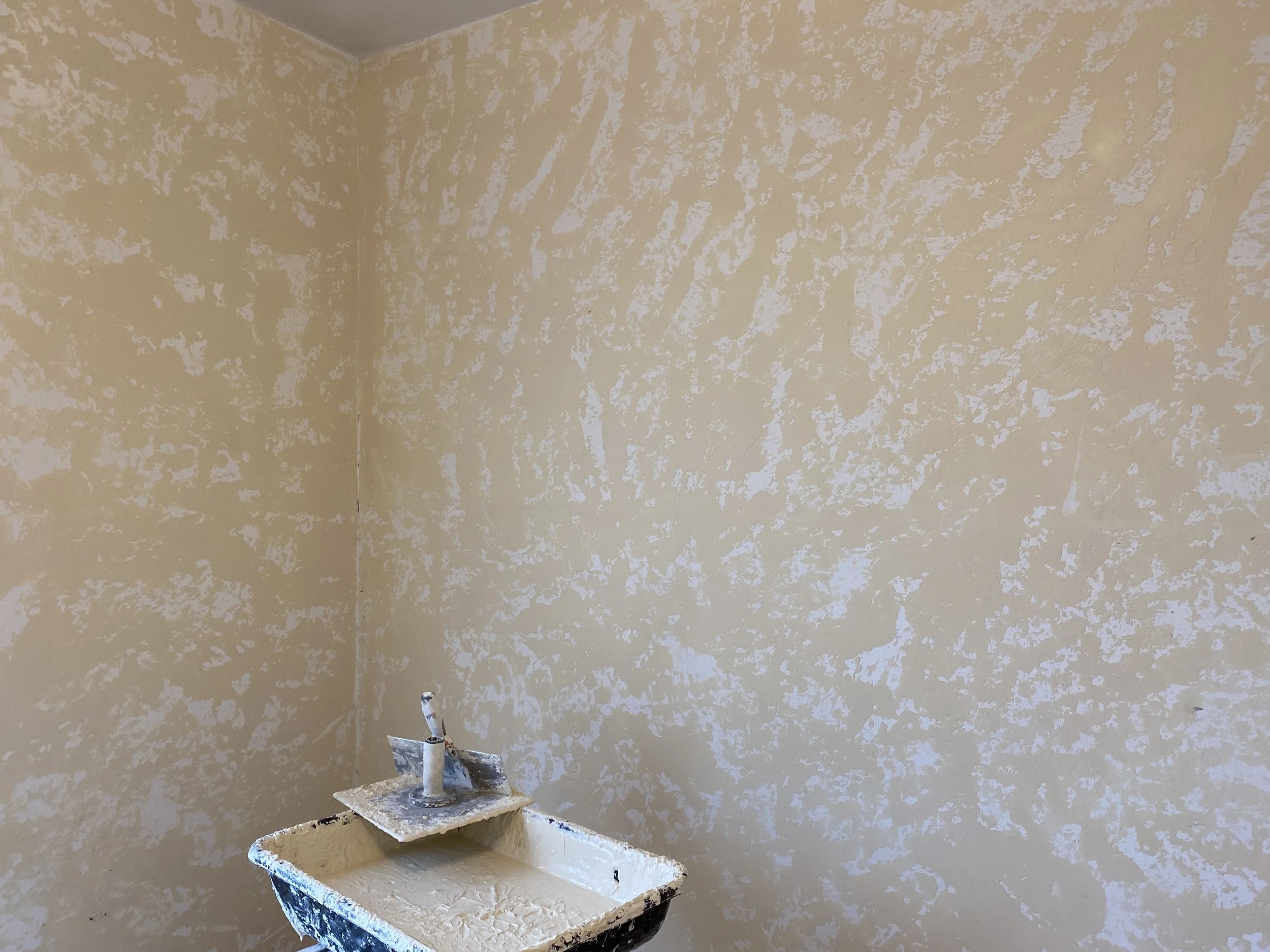 Interior wall with beige textured paint and a small utility sink with a faucet