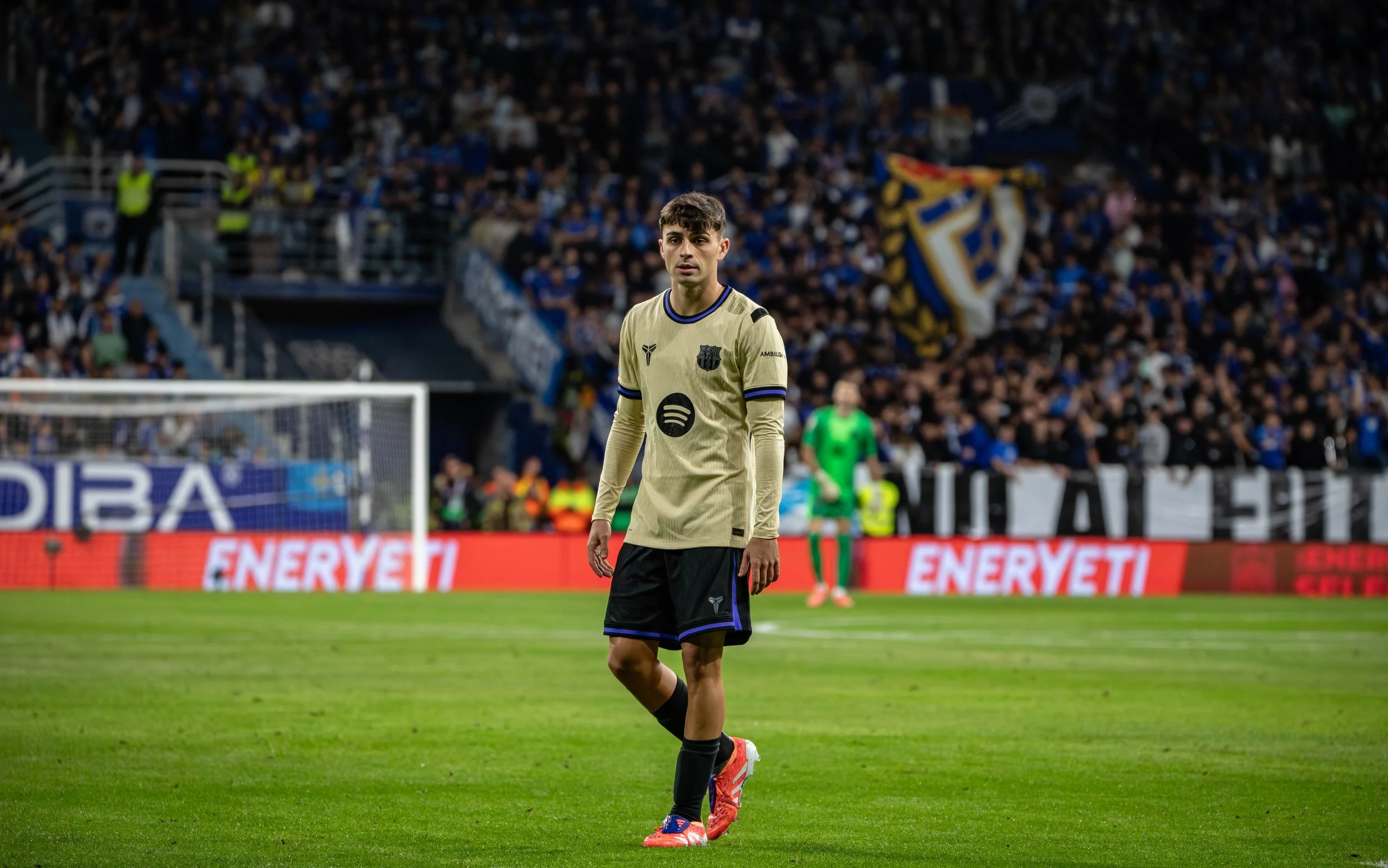 A football player standing on the field during a match, with fans in the background.