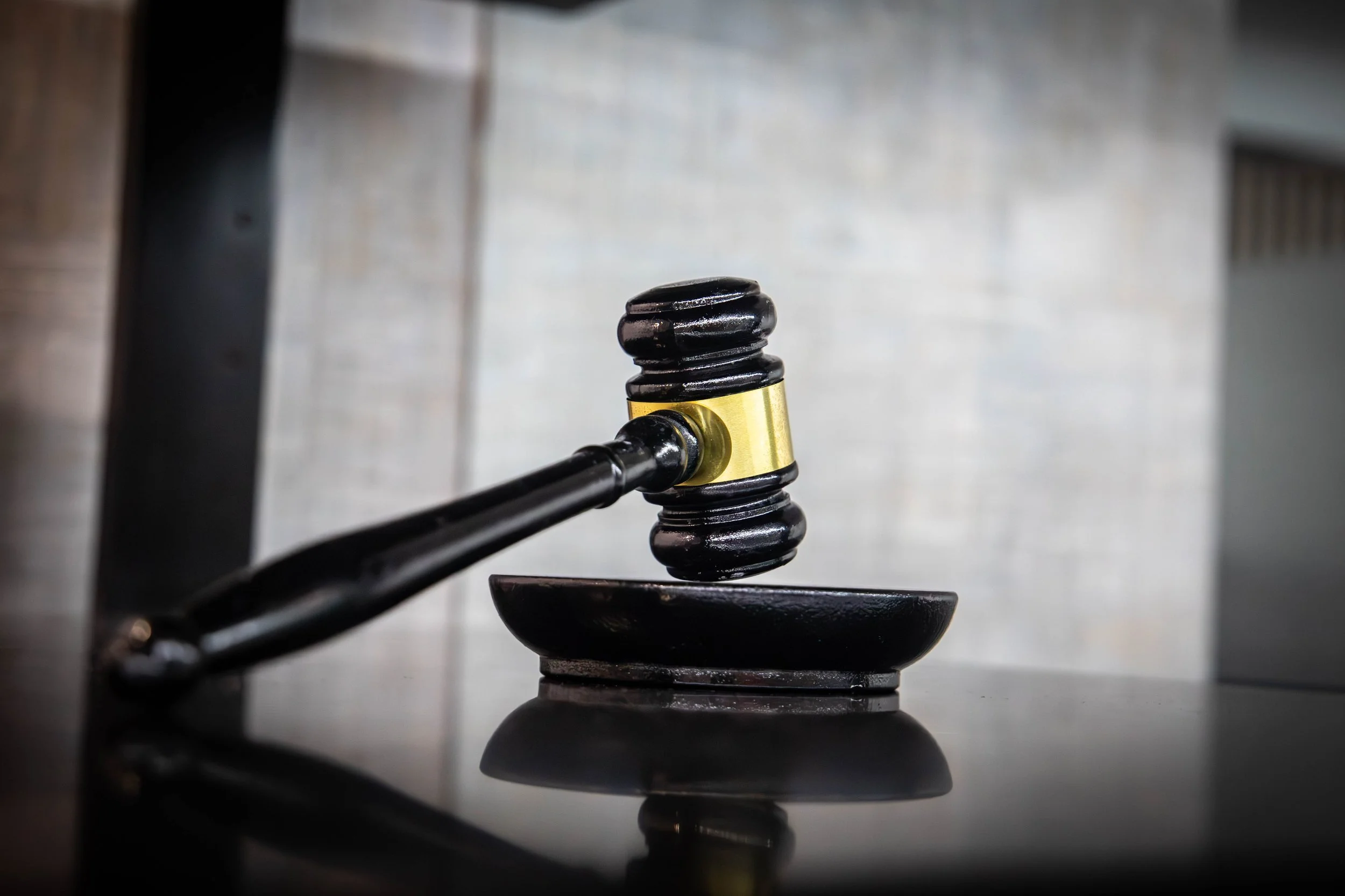Close-up of a wooden gavel with a gold band, resting on a sound block, with the gavel partially raised.